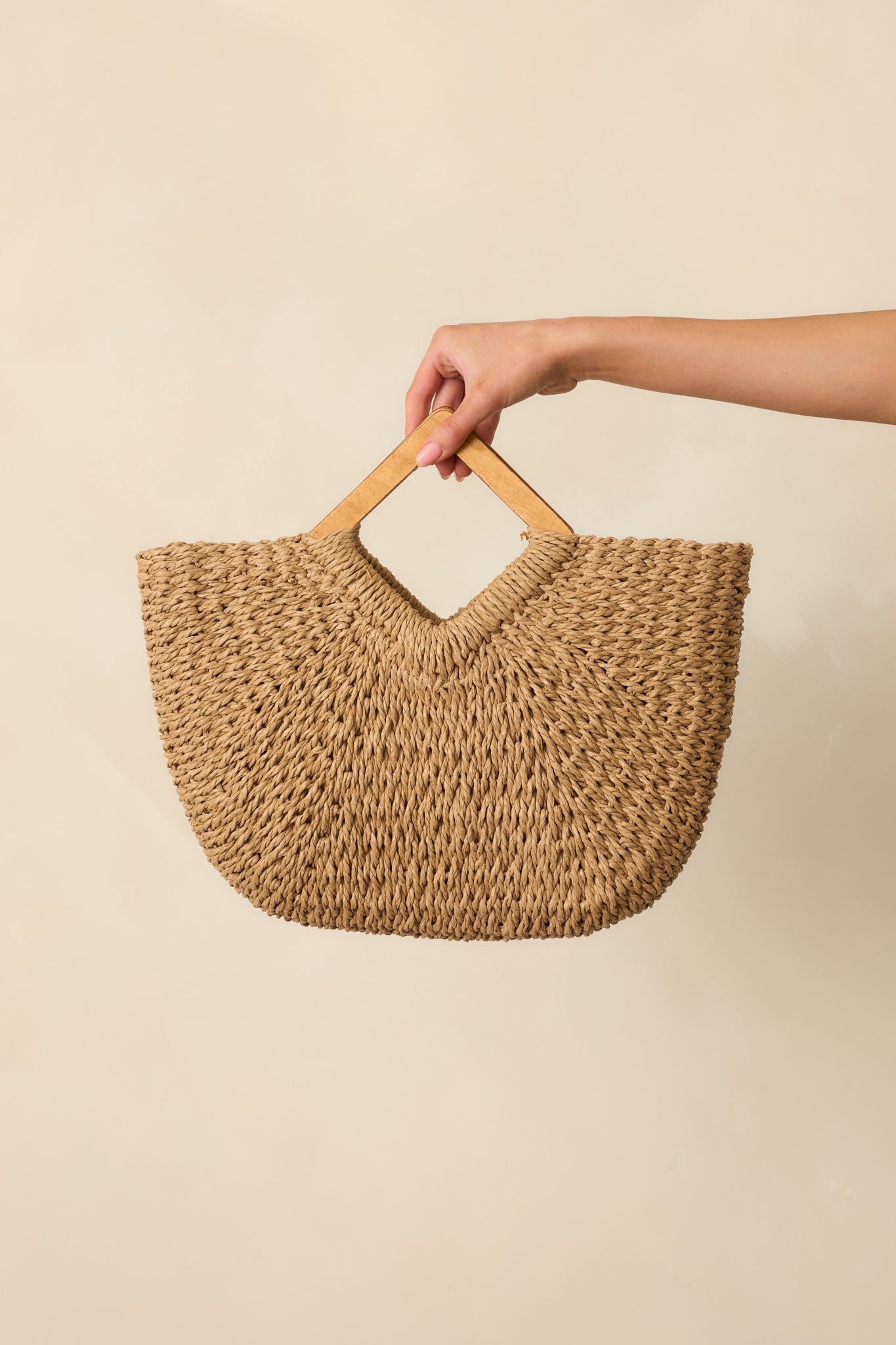 Tan woven raffia straw handbag with diamond-shaped wooden handles & structured base visible against a neutral background.