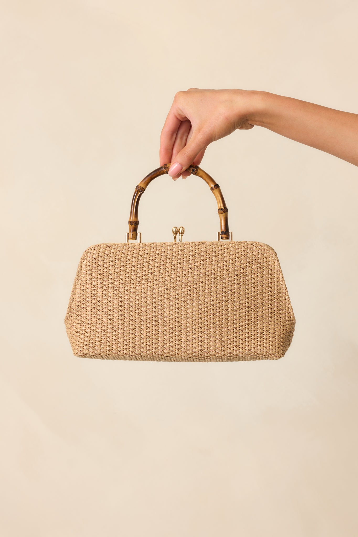 Full view of the ivory woven handbag featuring a structured brown bamboo handle and gold kiss lock clasp closure.