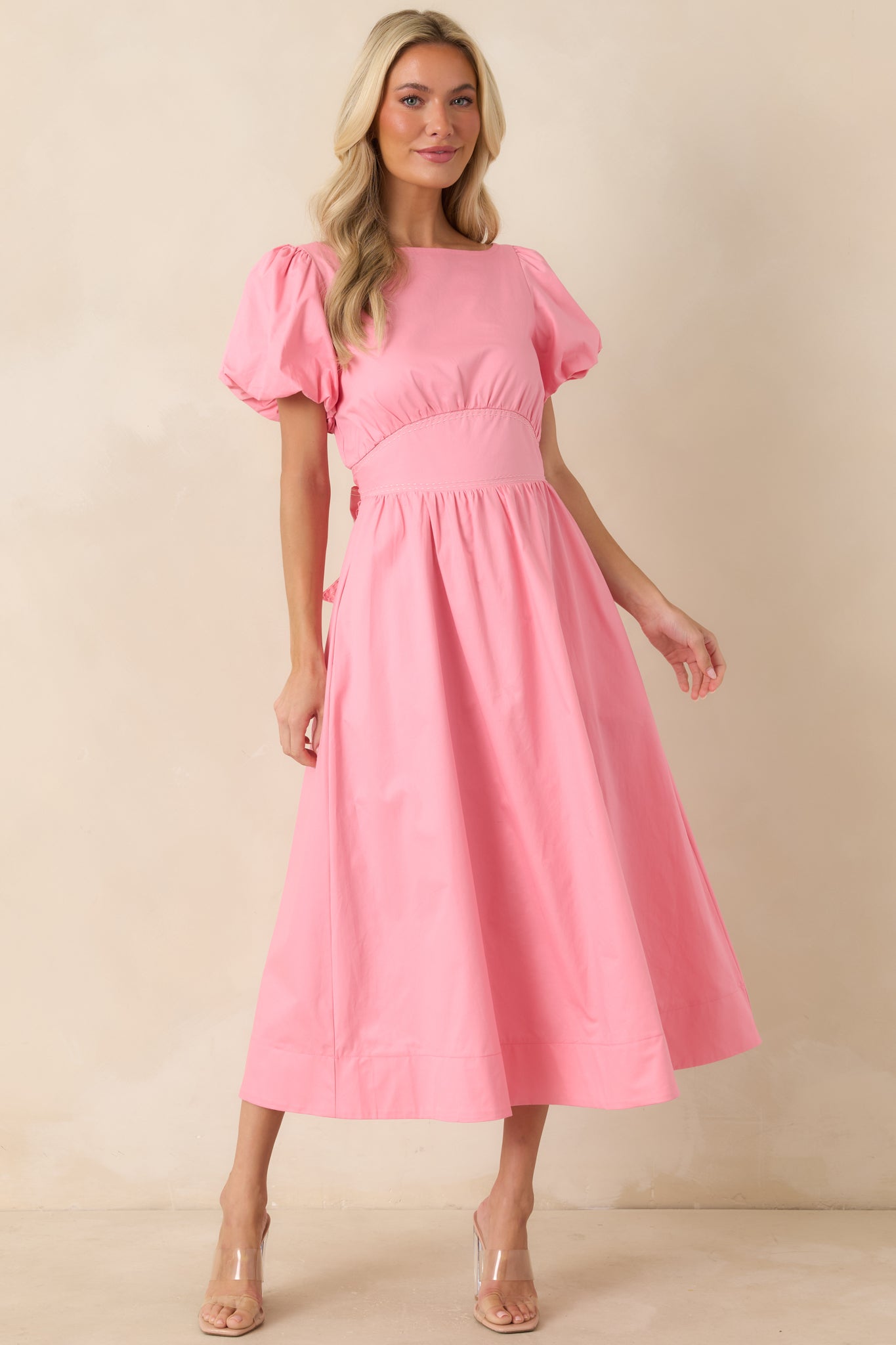 Pink cotton midi dress featuring puff sleeves with elastic cuffs, a fitted empire waist with contrast stitching, and a flowing midi-length skirt.