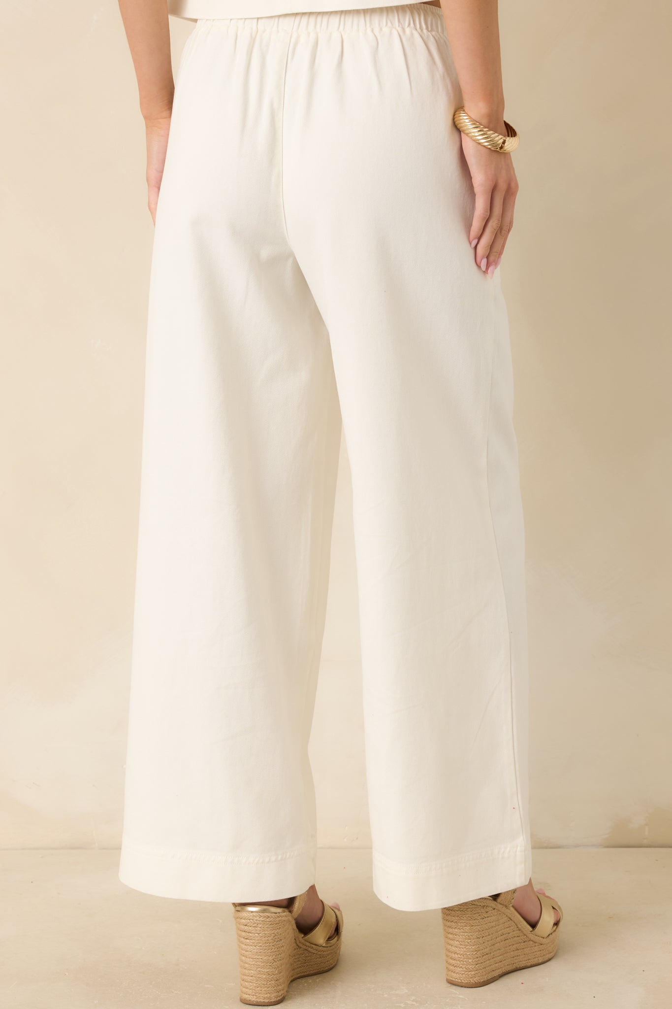 Rear view of the ivory wide-leg pants showing the elastic waistband and continuous relaxed drape through the full-length silhouette.