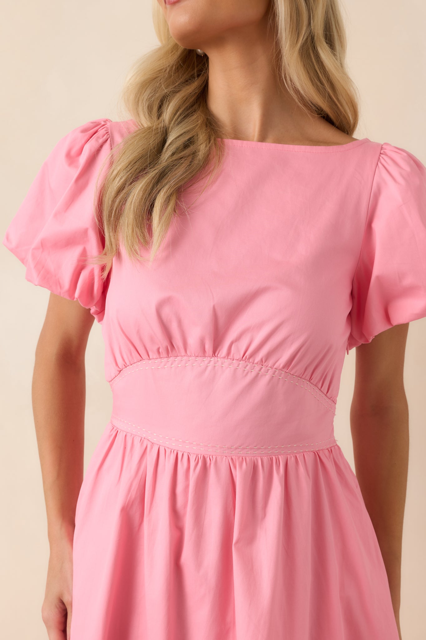 Close-up of the empire waistband showing contrast stitching and the removable self-tie sash detail on the pink cotton dress.
