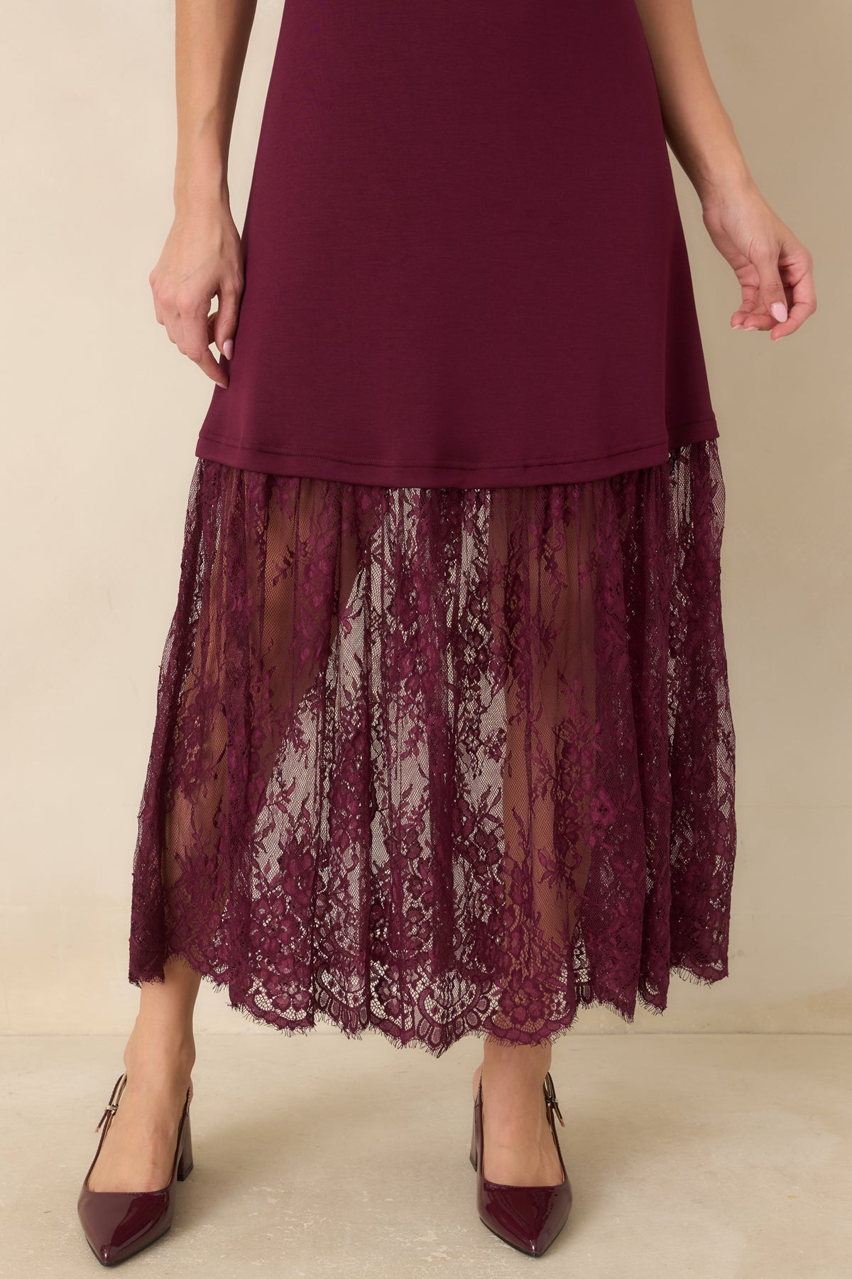 The plum knit dress features a gently flared floral lace skirt with a scalloped edge and a semi-sheer finish.
