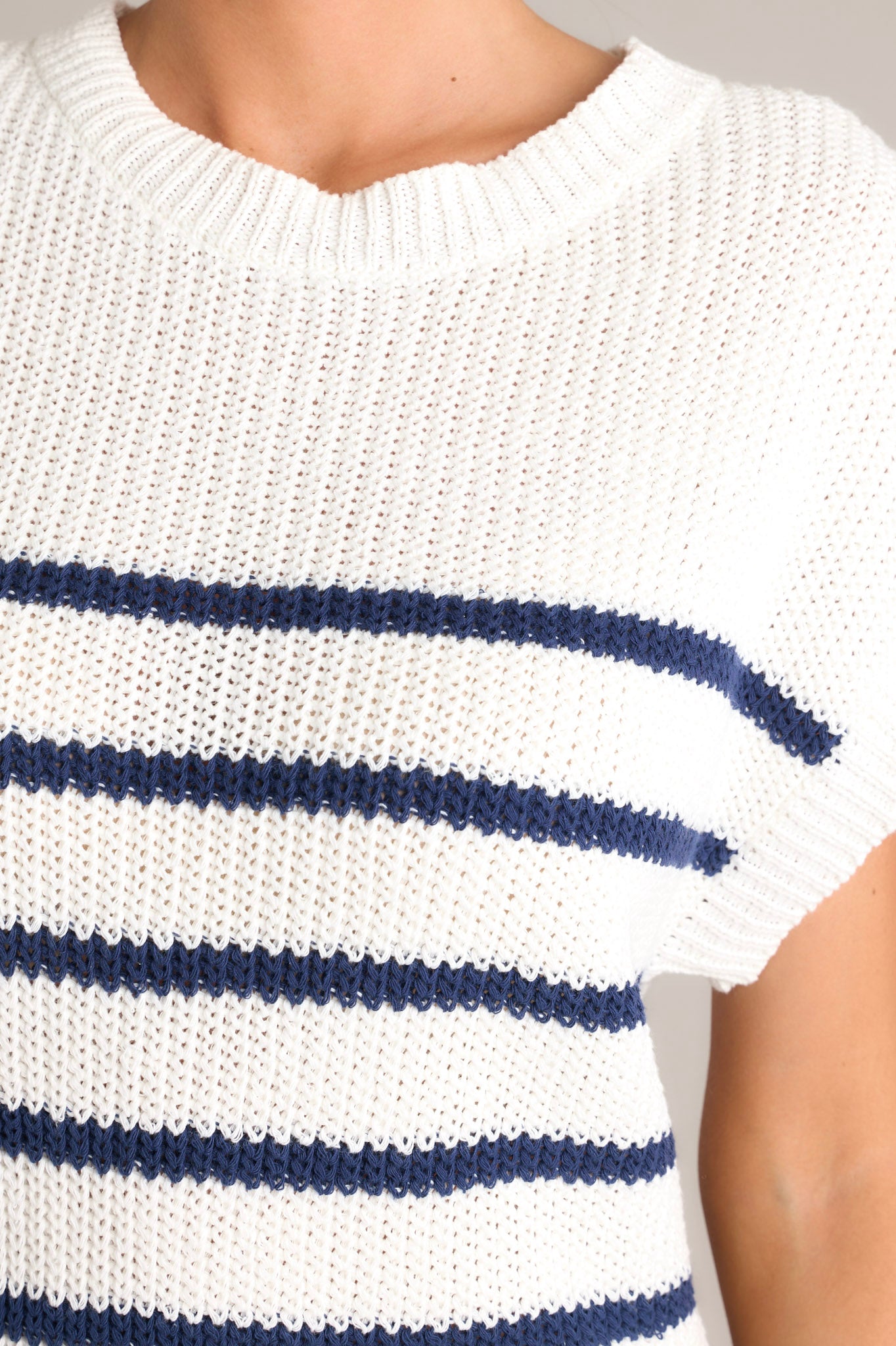 Close up view of this navy dress that features a crew neckline, a ribbed knitted bodice, horizontal stripes, and a solid flowy skirt.