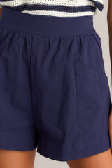Close up view of these shorts feature that a high waisted design, a thick waistband, an elastic insert at the back of the waist, and functional hip pockets.