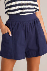 Angled close up front view of these shorts feature that a high waisted design, a thick waistband, an elastic insert at the back of the waist, and functional hip pockets.