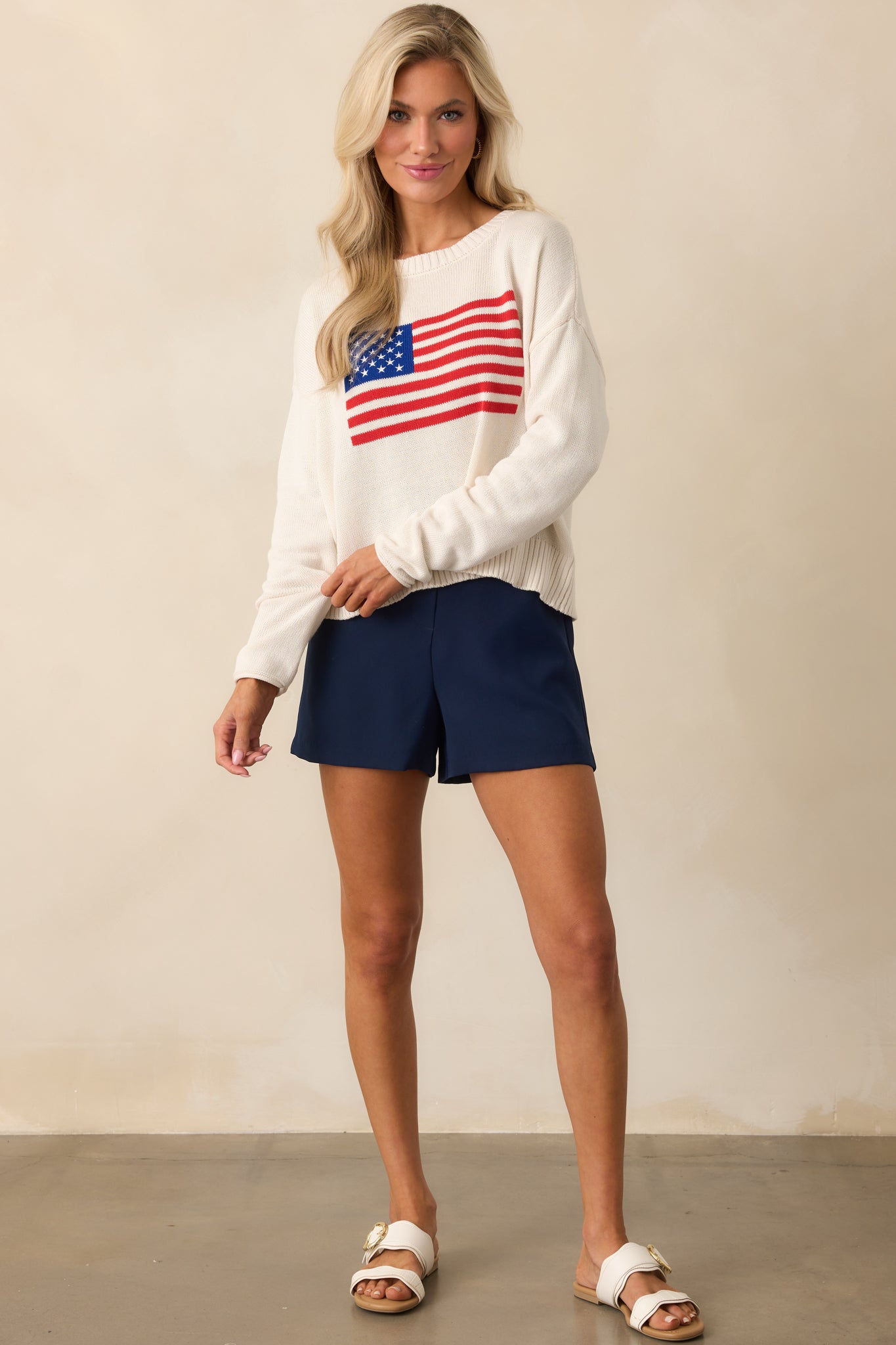 Ivory pullover sweater featuring a crew neck and bold flag embroidery across the bust, displayed in a full-frontal stance.