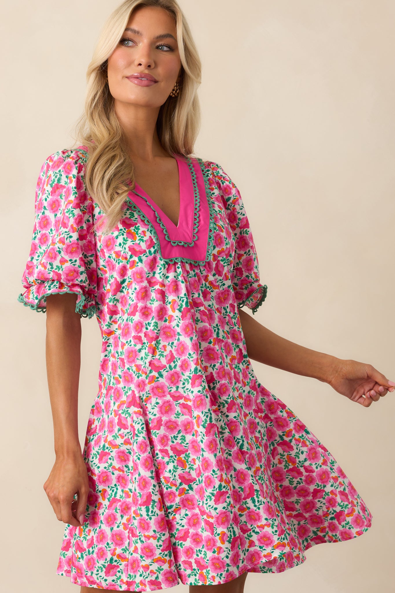 Focused shot of the hem of the pink mini dress, showing the green embroidered scalloped detail.