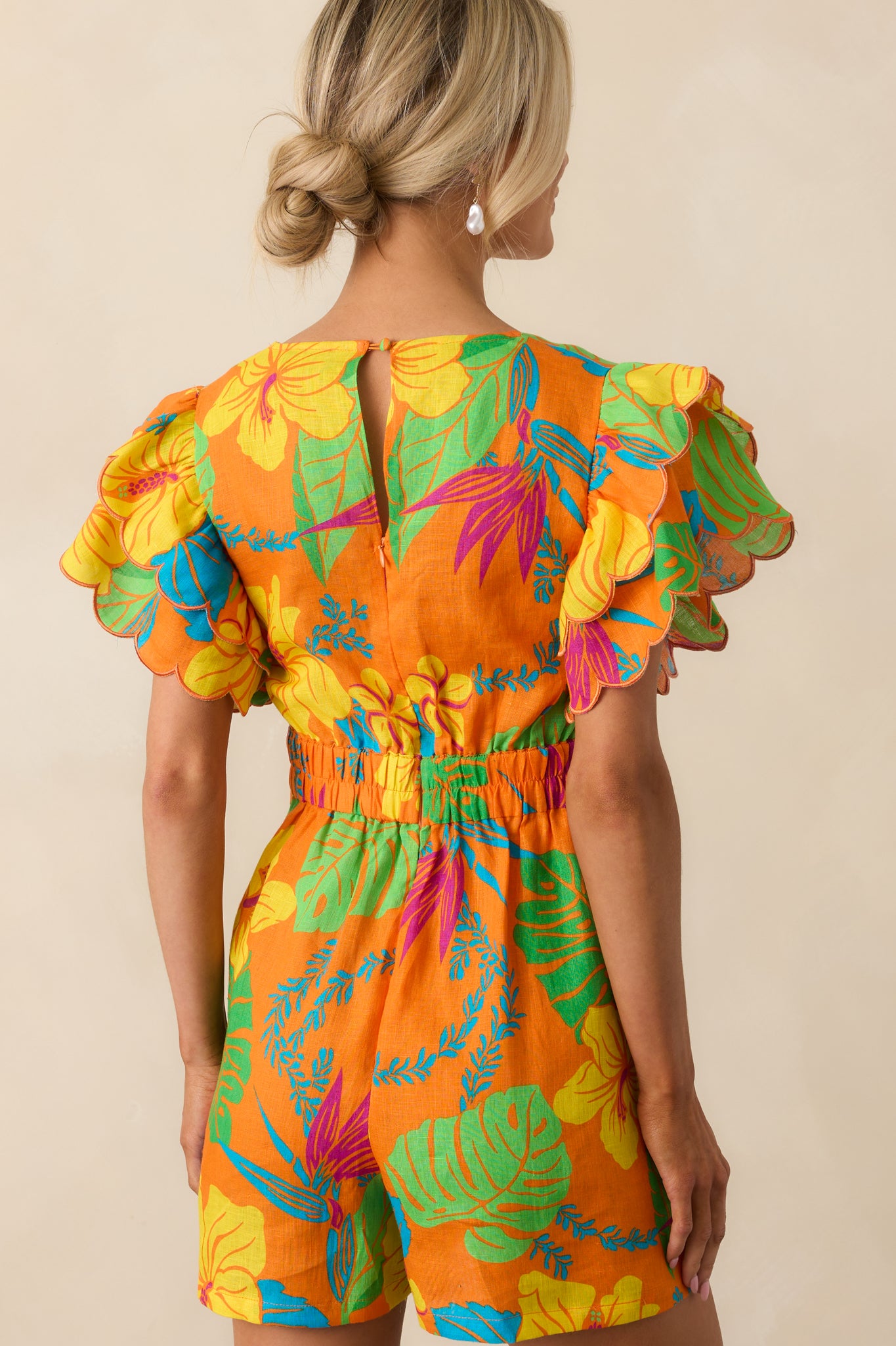 A view from behind showing the keyhole button closure, elastic waist insert, and hidden zipper of the romper.