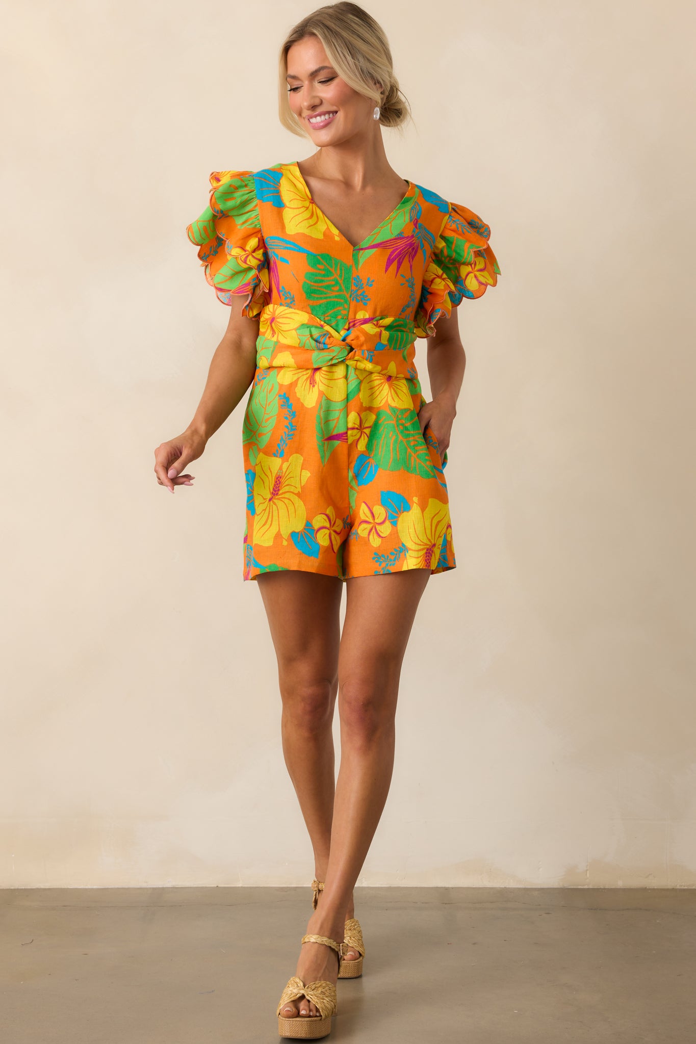 Full-length image showing the scallop hem flutter sleeves and relaxed fit of the linen tropical romper.