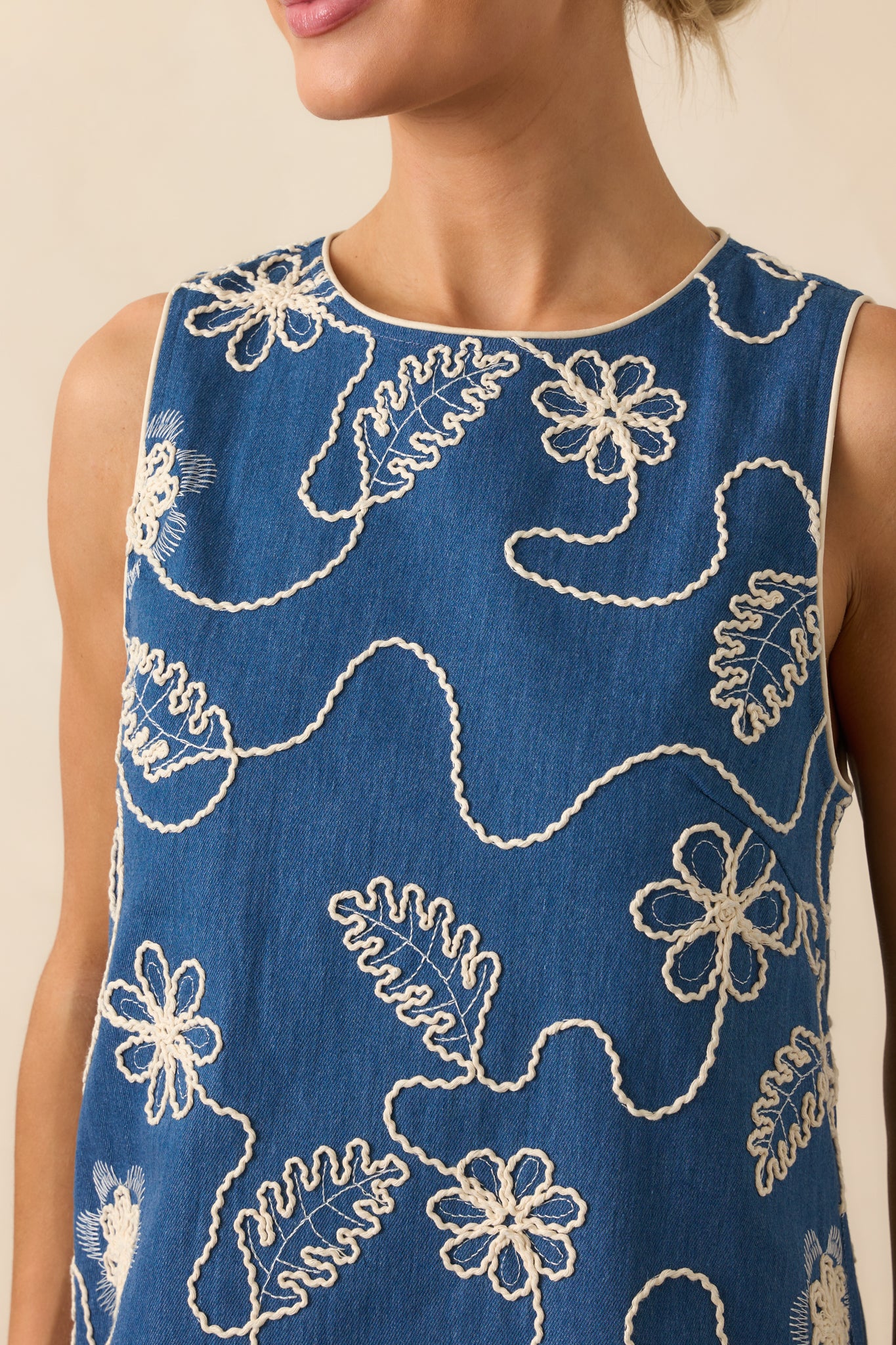 Tight detail of the ivory floral embroidery and piping on the dark denim-like fabric, highlighting texture and craftsmanship.