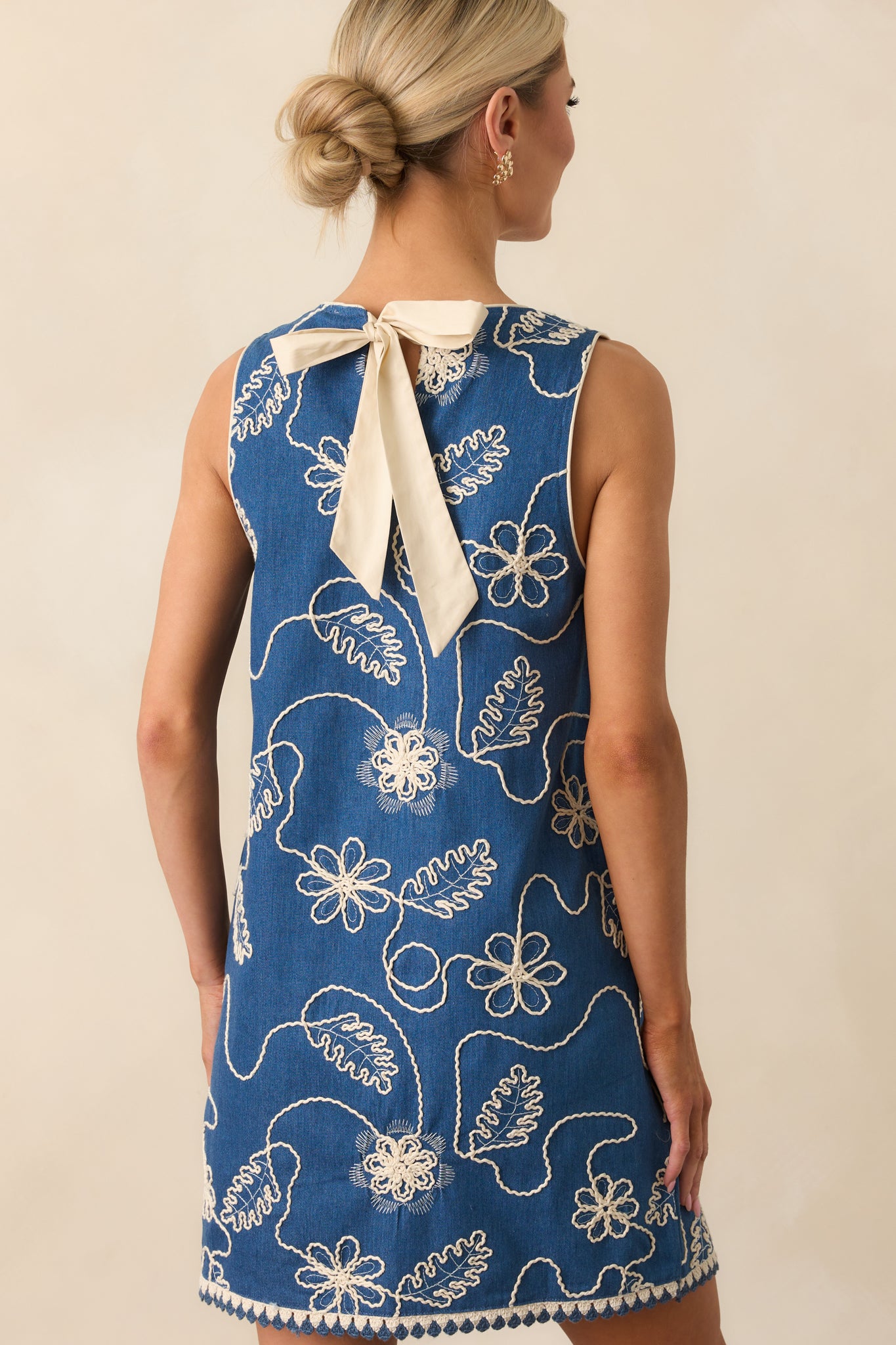 Rear view of the dress showing the adjustable self-tie back bow and keyhole closure at the neckline, framed by clean piping trim.