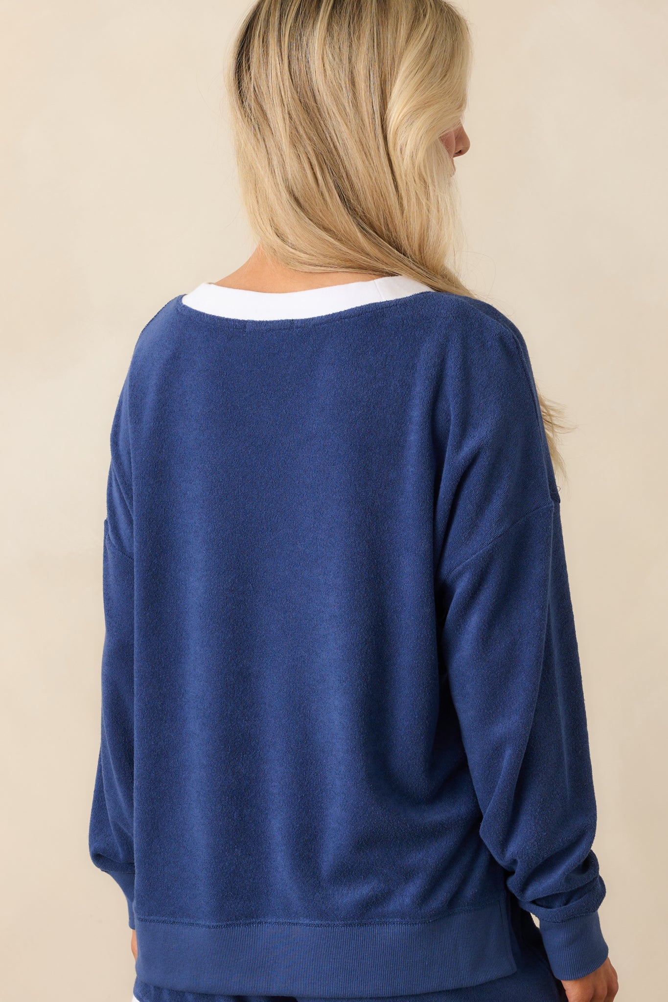 A complete back view of the blue sweatshirt showcasing its overall relaxed fit and ribbed hemline.
