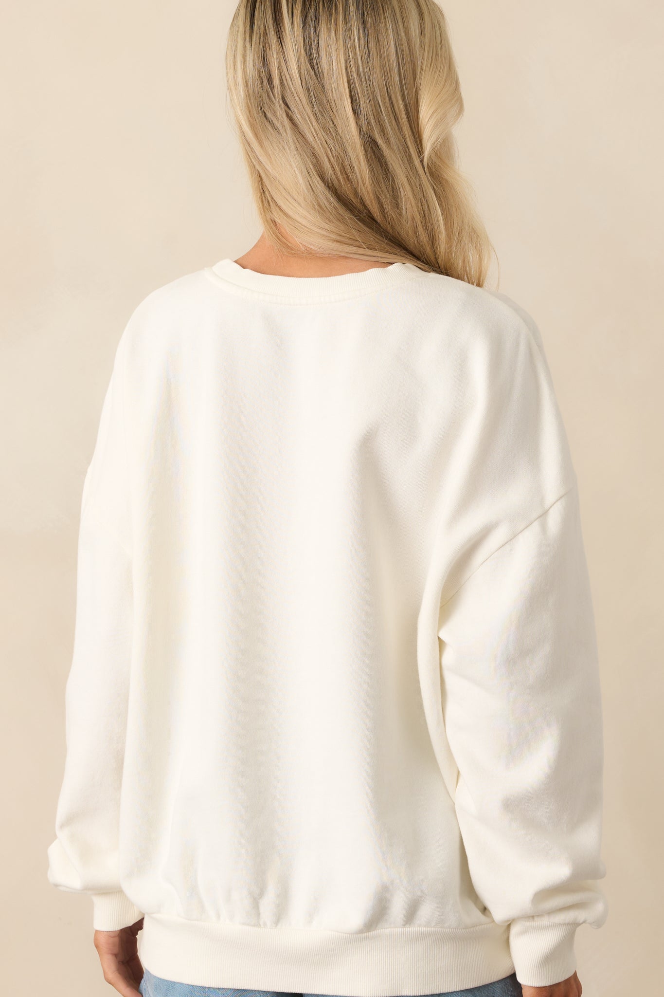 A view from behind of the ivory sweatshirt highlighting the plain back design, oversized fit, and long sleeves.