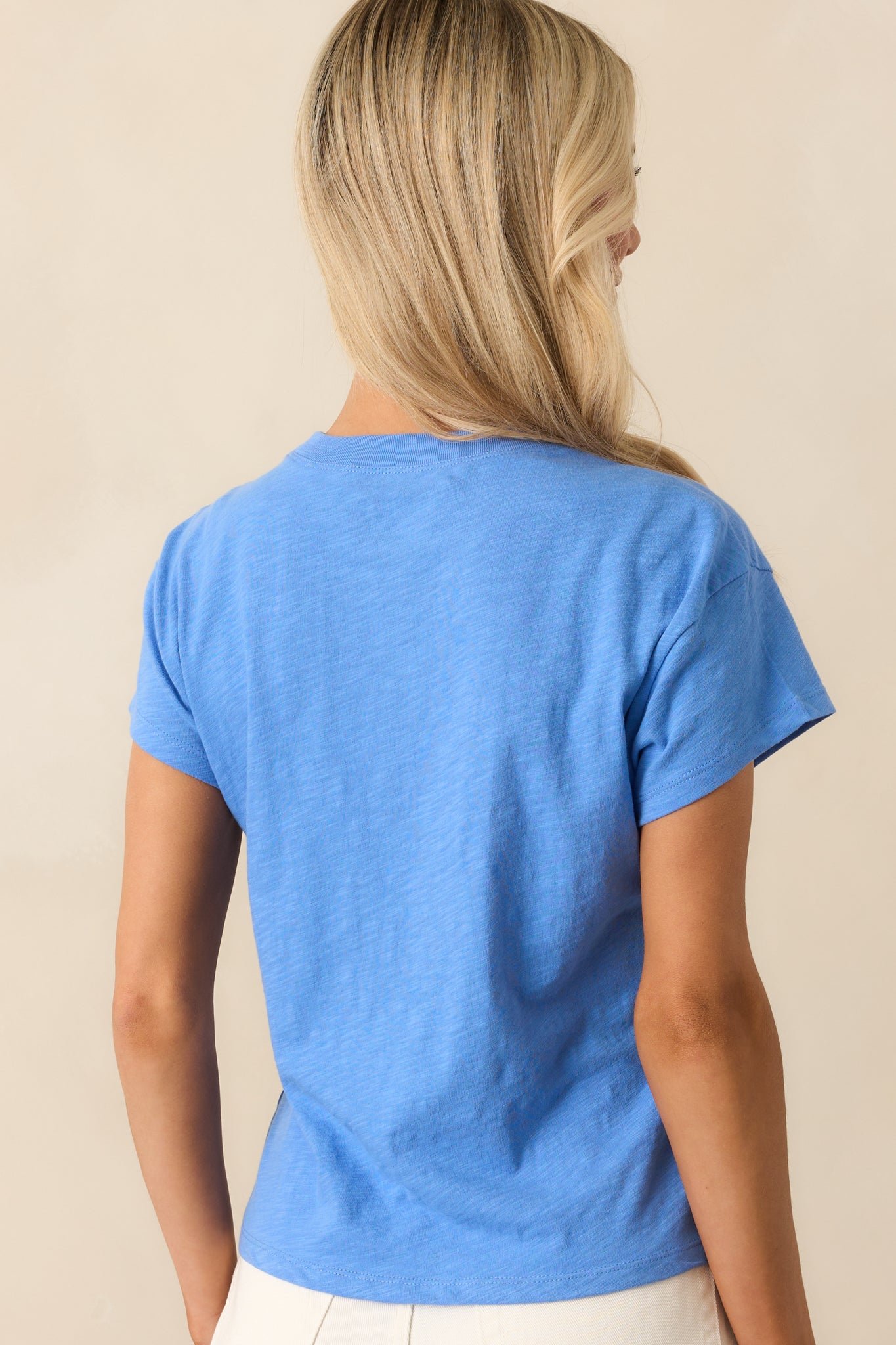 A back view of the blue tee displaying
its straight hem and back neckline construction.