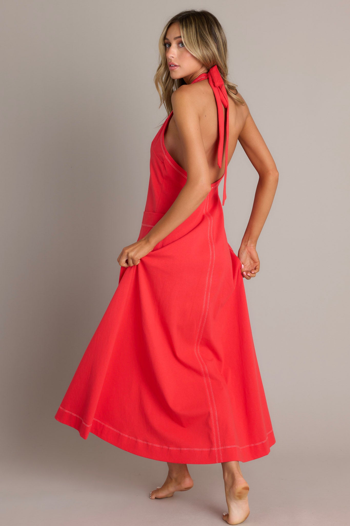 Angled back view of this Casual red maxi dress with contrast stitching, V-neck, and large front pockets.