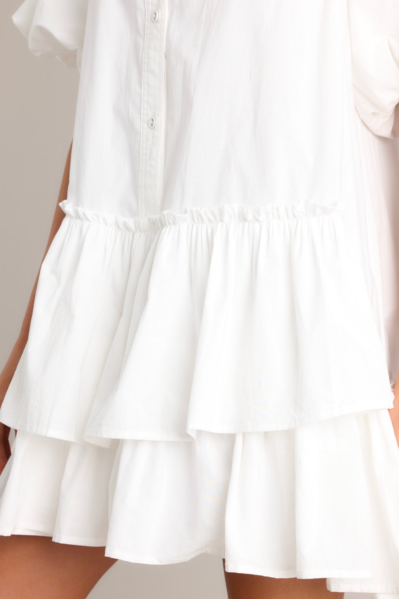 Close-up of a white tiered mini dress, featuring a button-down front, ruffled layers, and a flouncy skirt