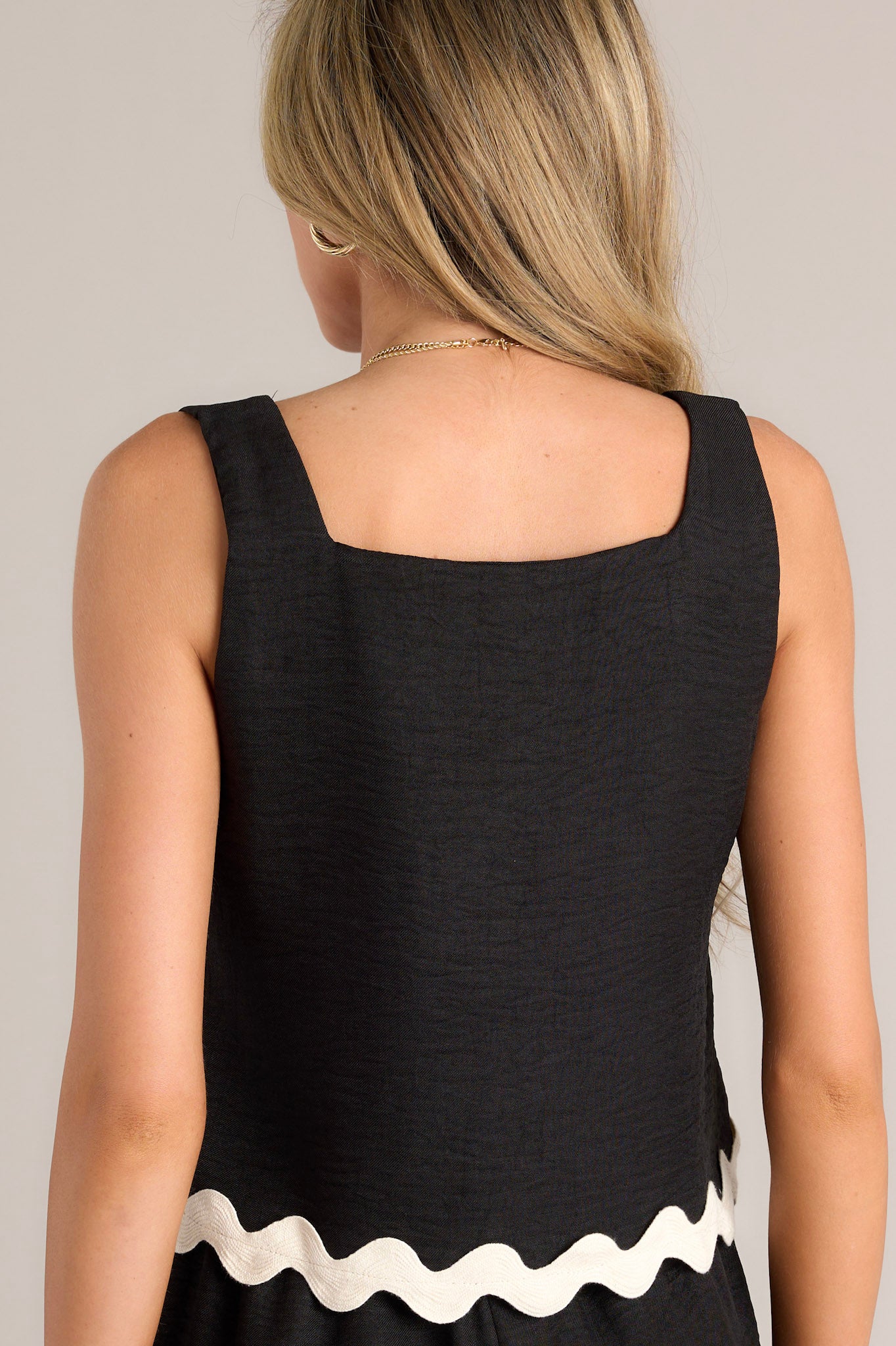 Back view of this black tank top that features a square neckline, wide straps, a boxy fit, and a scalloped detail at the hem.