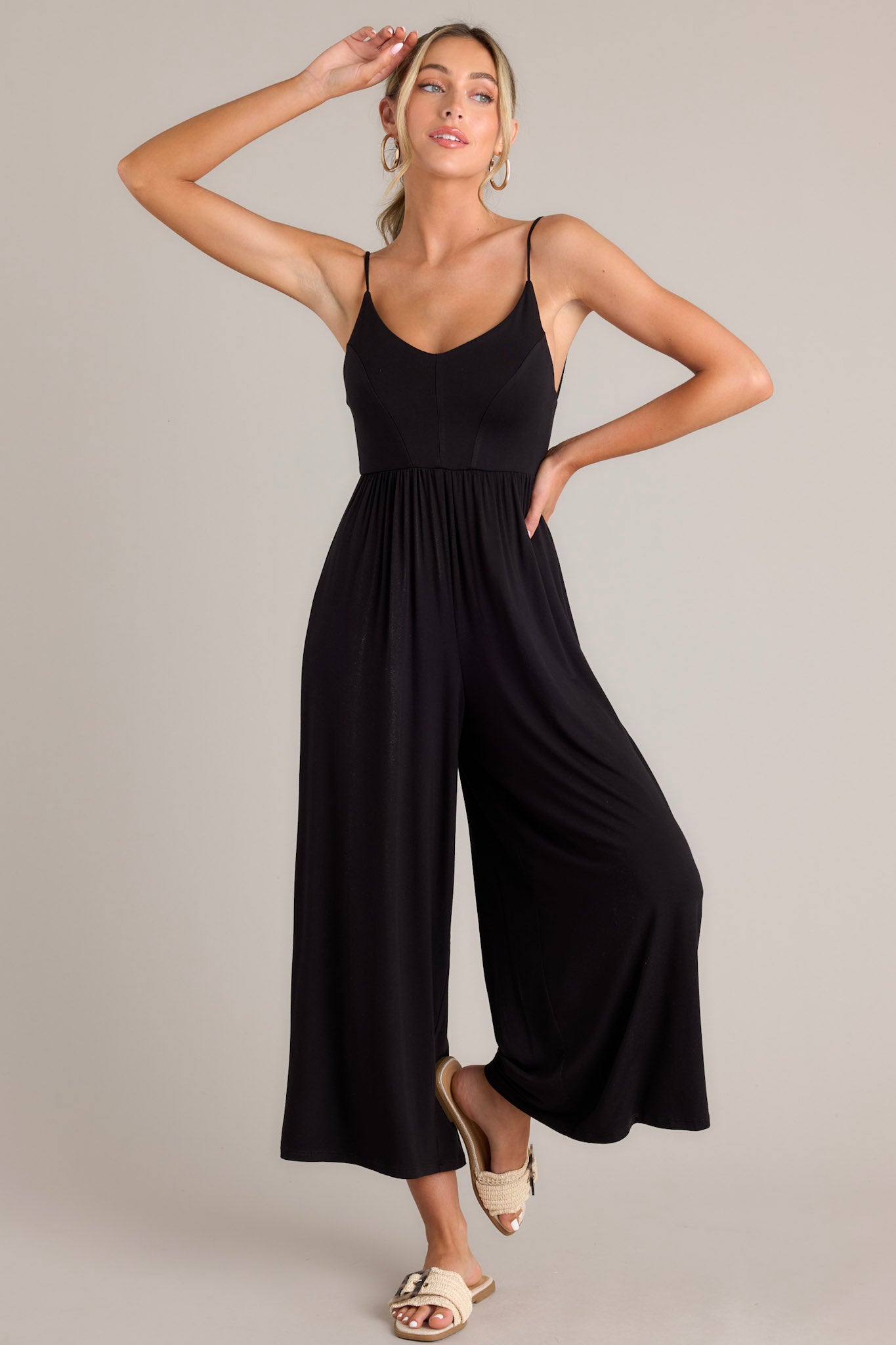 This black jumpsuit features a v-neckline, thin adjustable straps that cross in the back, an elastic waistband, and a wide leg.