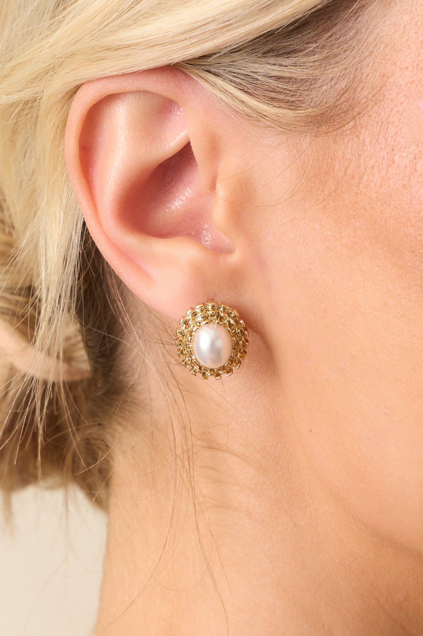 Extreme close-up of one earring focusing on the smooth ivory faux pearl and the fine texturing of the surrounding gold oval halo.