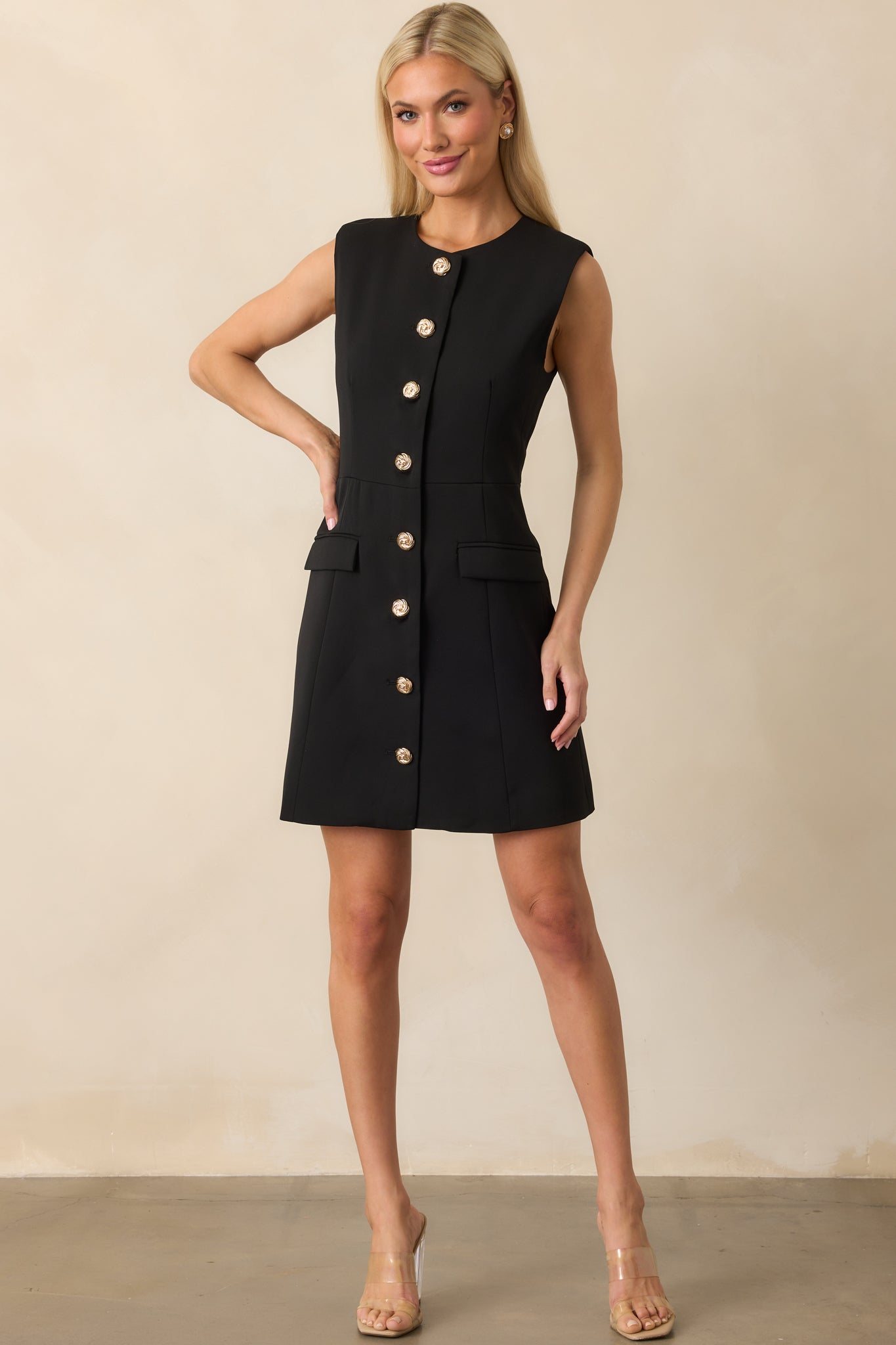 Full body view of the black mini dress showcasing its tailored silhouette and sleeveless cut with gold button front closure.