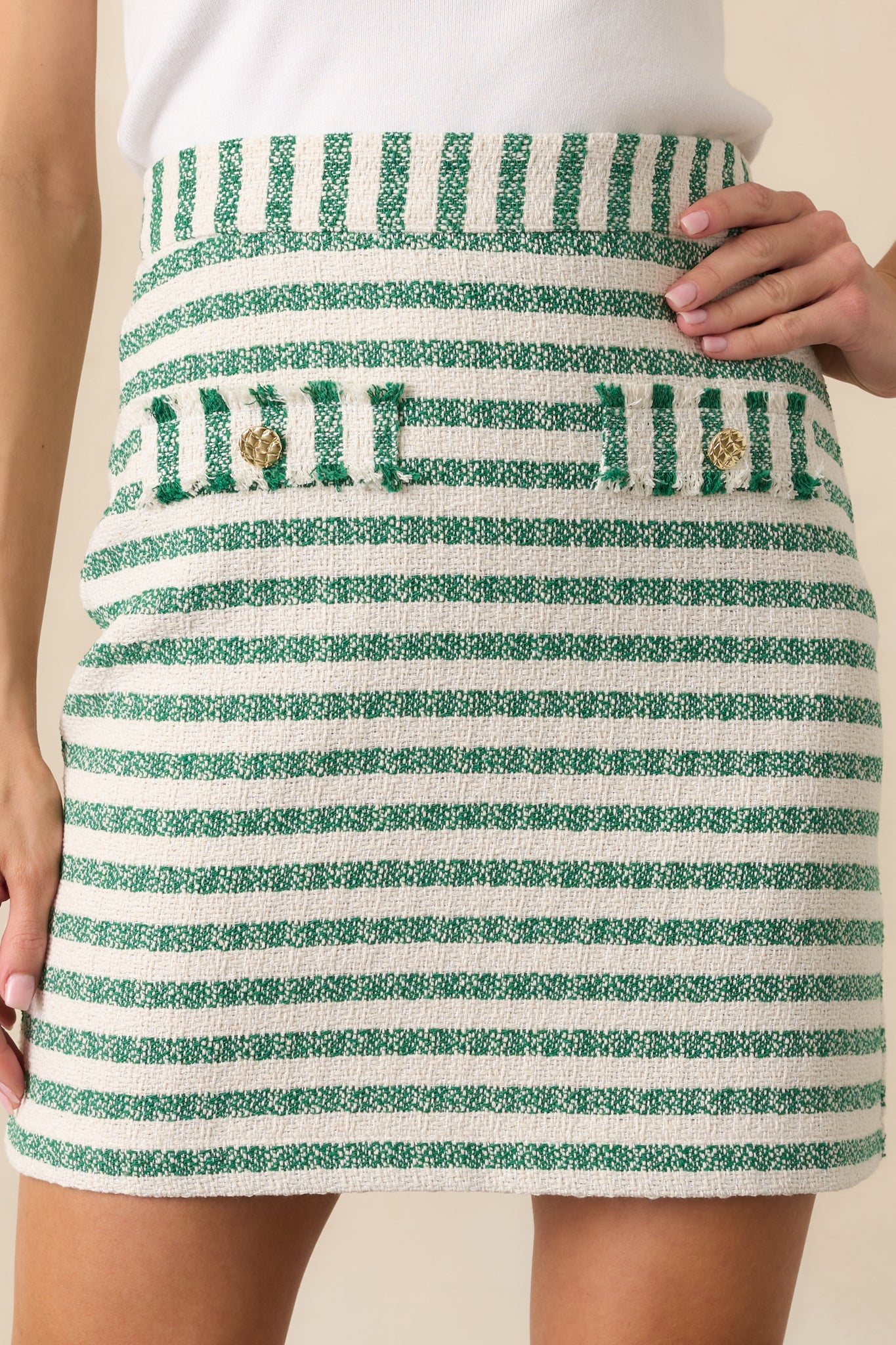 Close-up of the bouclé texture, gold button detail, and the edge of a raw hem pocket.