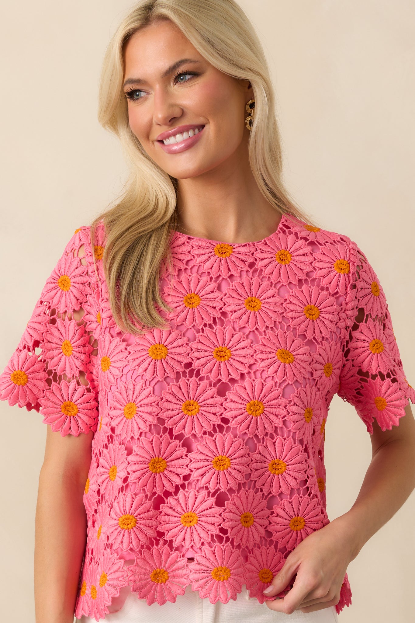 Up-close photo of modeling wearing a pink and orange floral embroidered lace overlay, hot pink lining, daisy petal scalloped hems, round neckline, short sleeves, an open self-tie bow back design, and a relaxed fit.