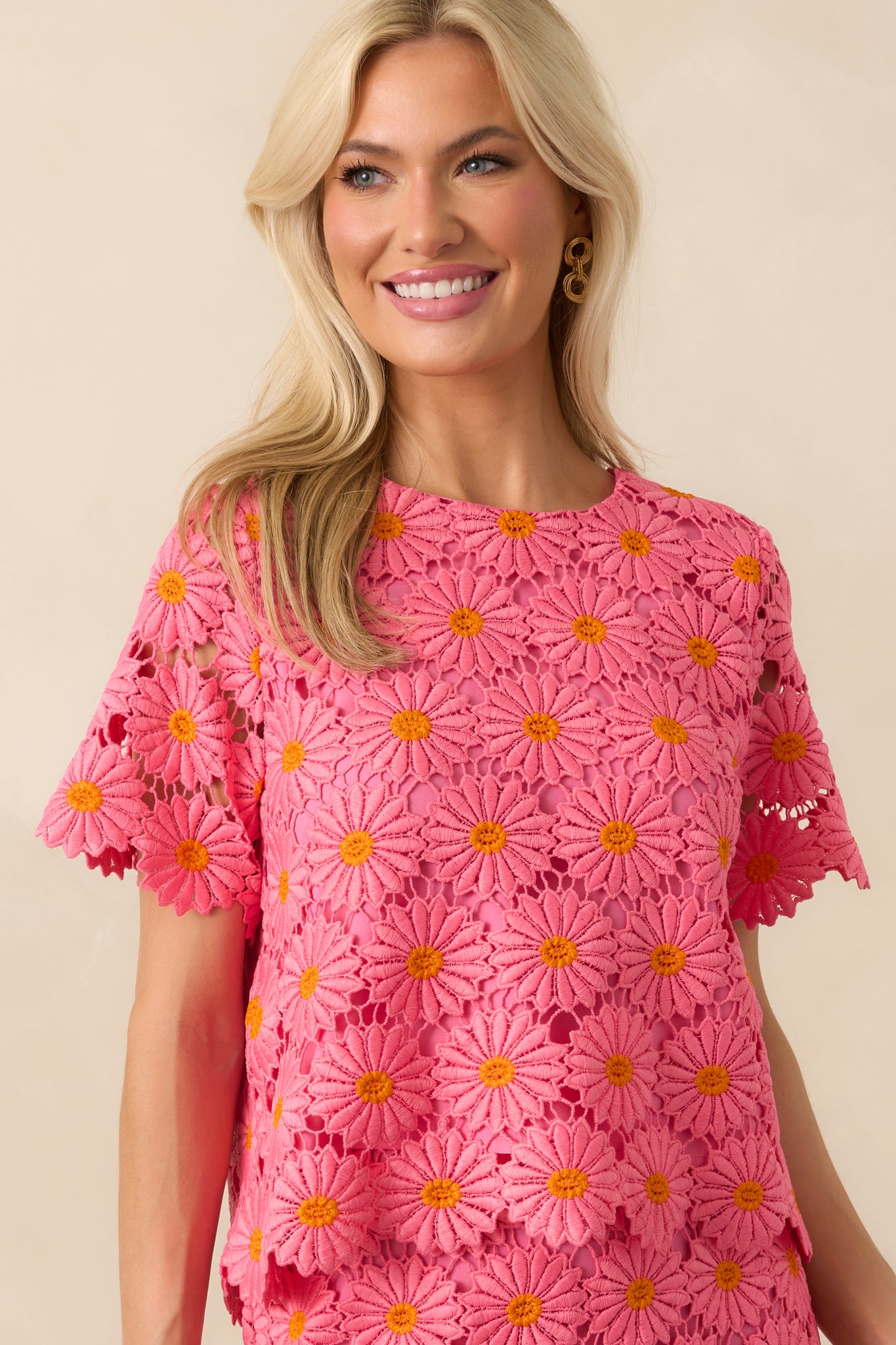 Up-close photo of modeling wearing a pink and orange floral embroidered lace overlay, hot pink lining, daisy petal scalloped hems, round neckline, short sleeves, an open self-tie bow back design, and a relaxed fit.