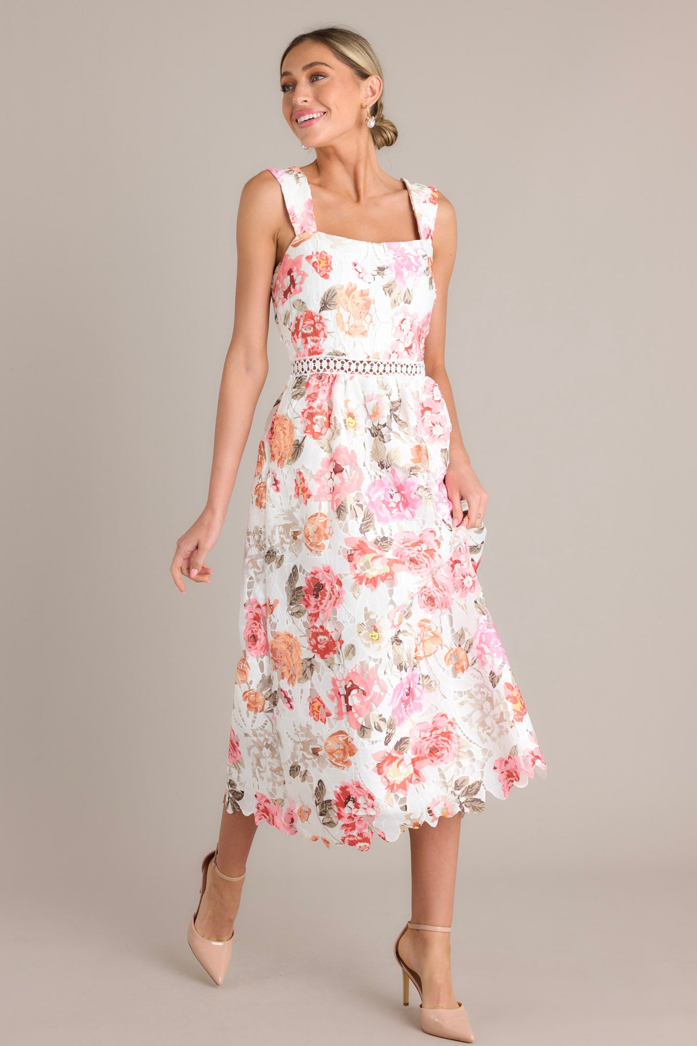 This dress features a square neckline, fitted bodice, crocheted cinched waist, functional pockets, and a full lace mid-length skirt in a white multi floral pattern.