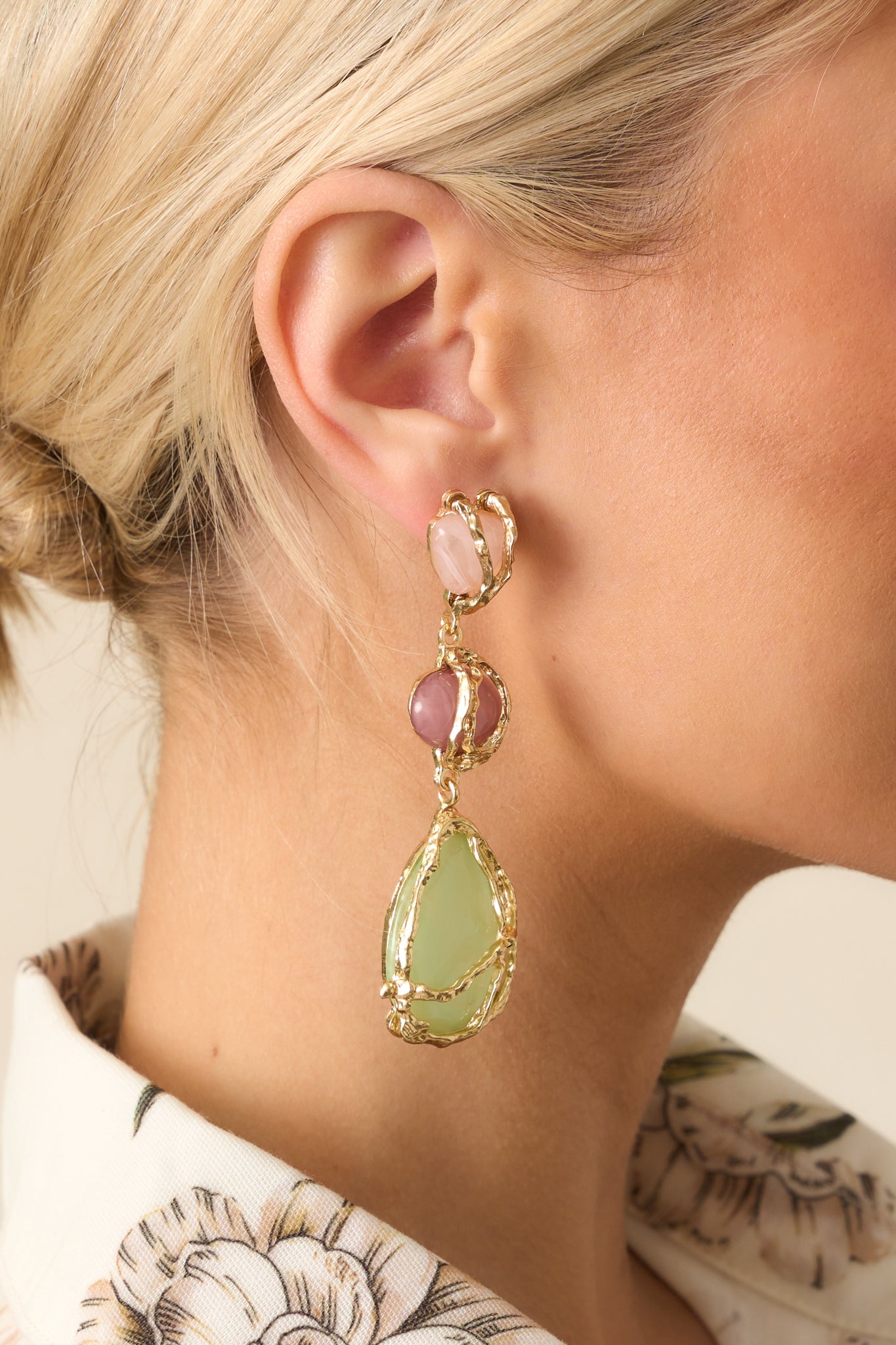Cropped view of the earrings showing the pink, mauve, and light green stones arranged in increasing size with a sculptural gold wrap design.