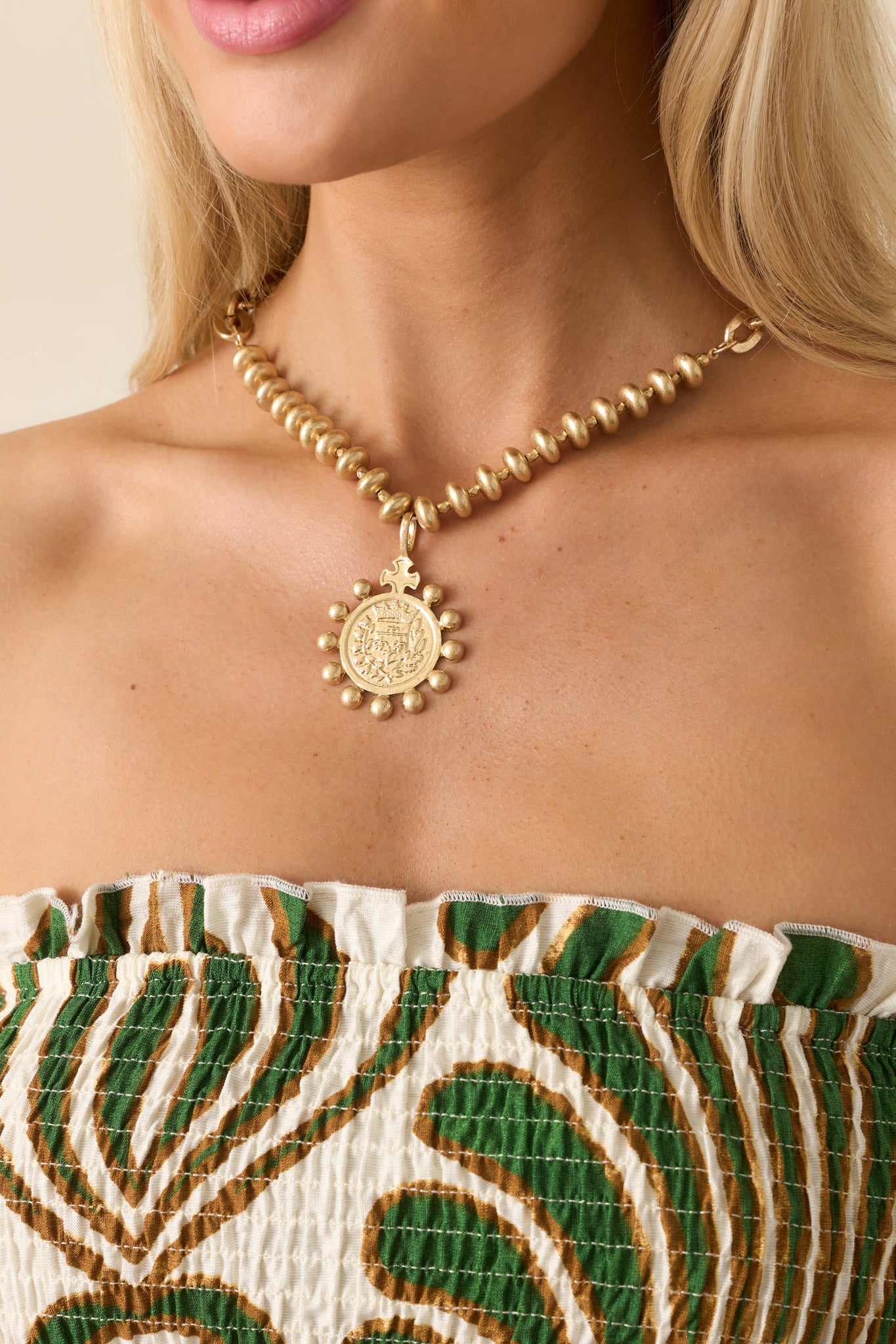 Cropped shot highlighting the large medallion pendant with an embossed crest and granulated bead border.