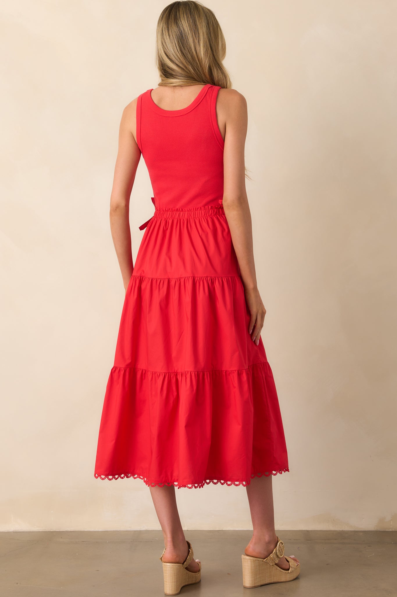A view from behind of the red midi dress with a tiered skirt, scalloped hem, and pockets slightly visible from the side.