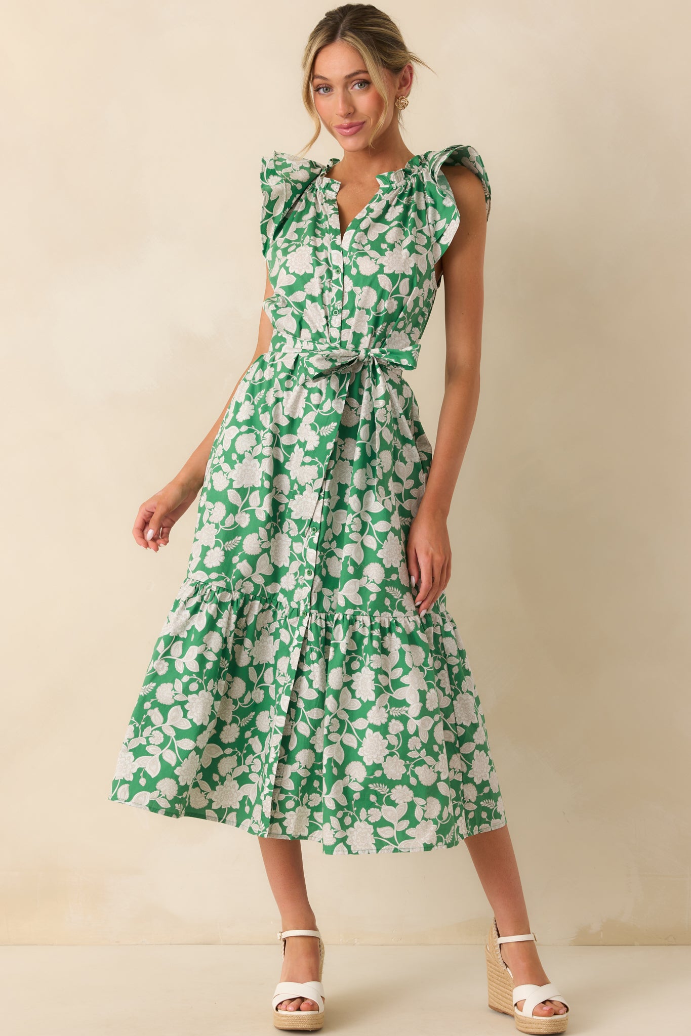 Model wearing a green maxi dress that features a ruffle notch v-neckline, layered flutter sleeves, functional button front, optional self-tie belt, 100% cotton fabric, bottom tiered skirt, and functional pockets.