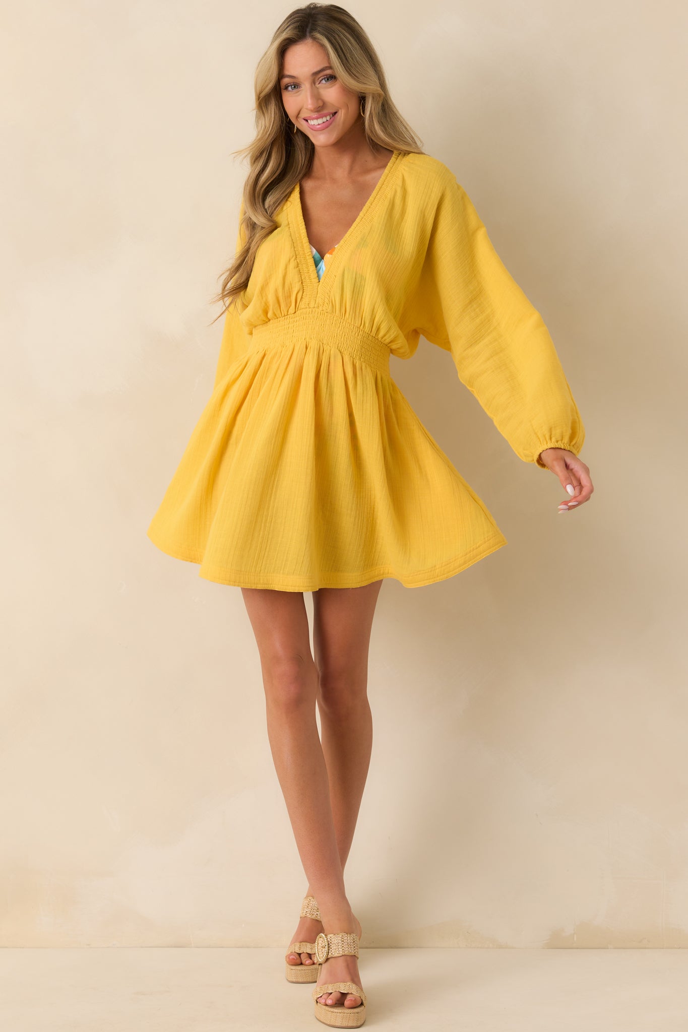 The yellow mini dress made of lightweight cotton gauze, featuring a smocked v-neckline and long dolman sleeves.
