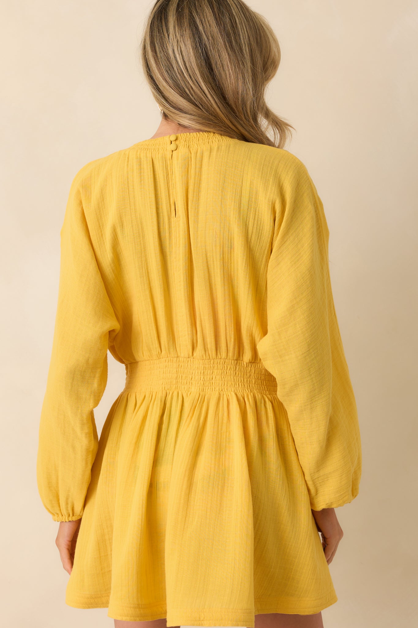 A back view of the yellow mini dress showcasing the keyhole button closure and gathered waist.