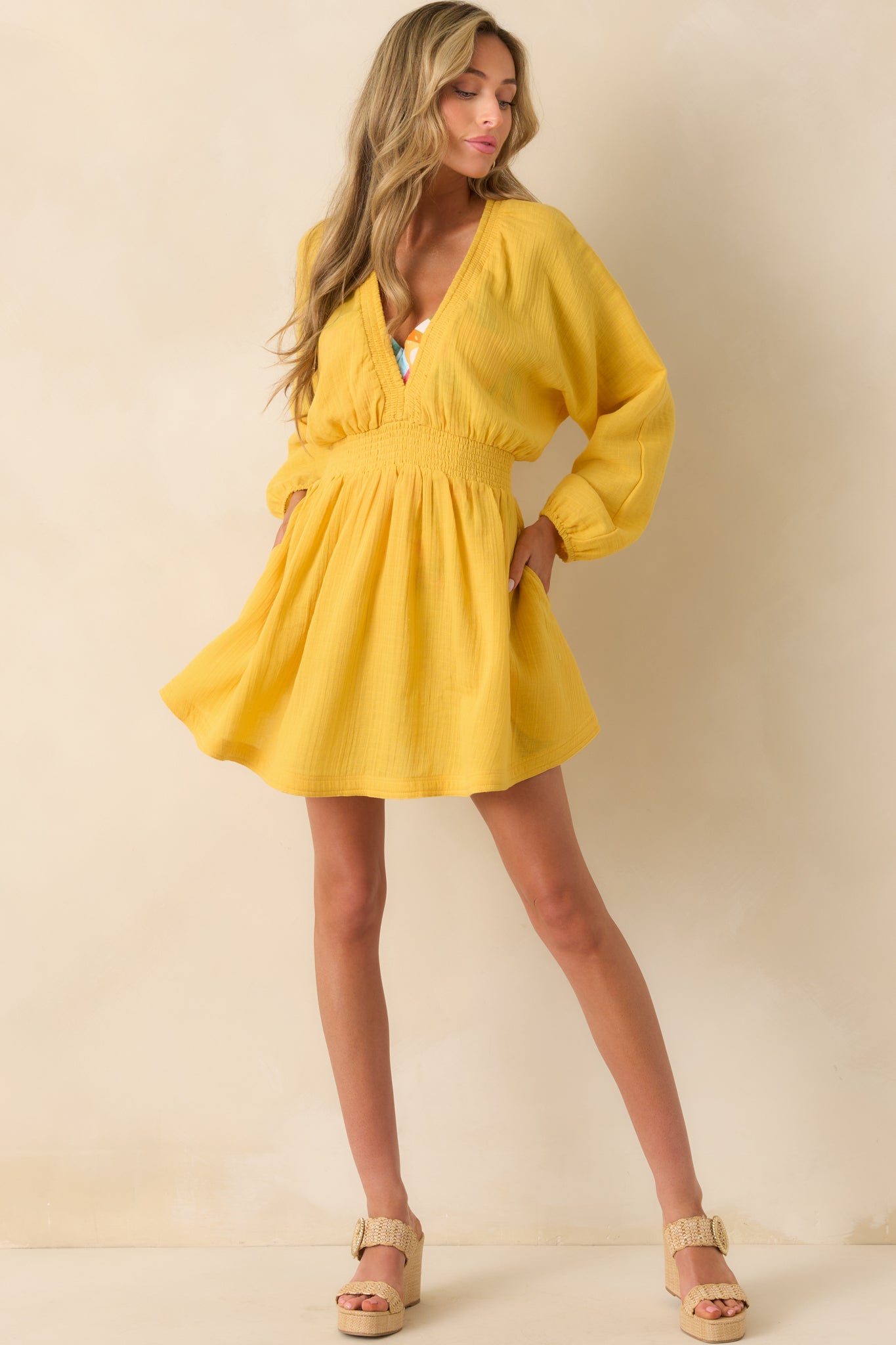 A complete profile of the flowy yellow dress highlighting its functional side pockets and airy long sleeves.