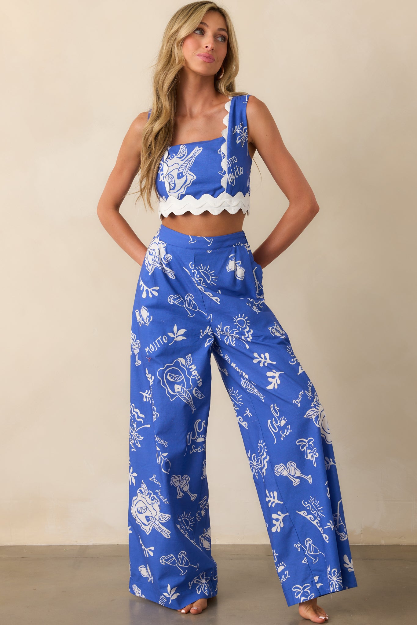 Blue high-waisted pants with wide legs shown in full view, highlighting the structured pleated front and elongated silhouette.