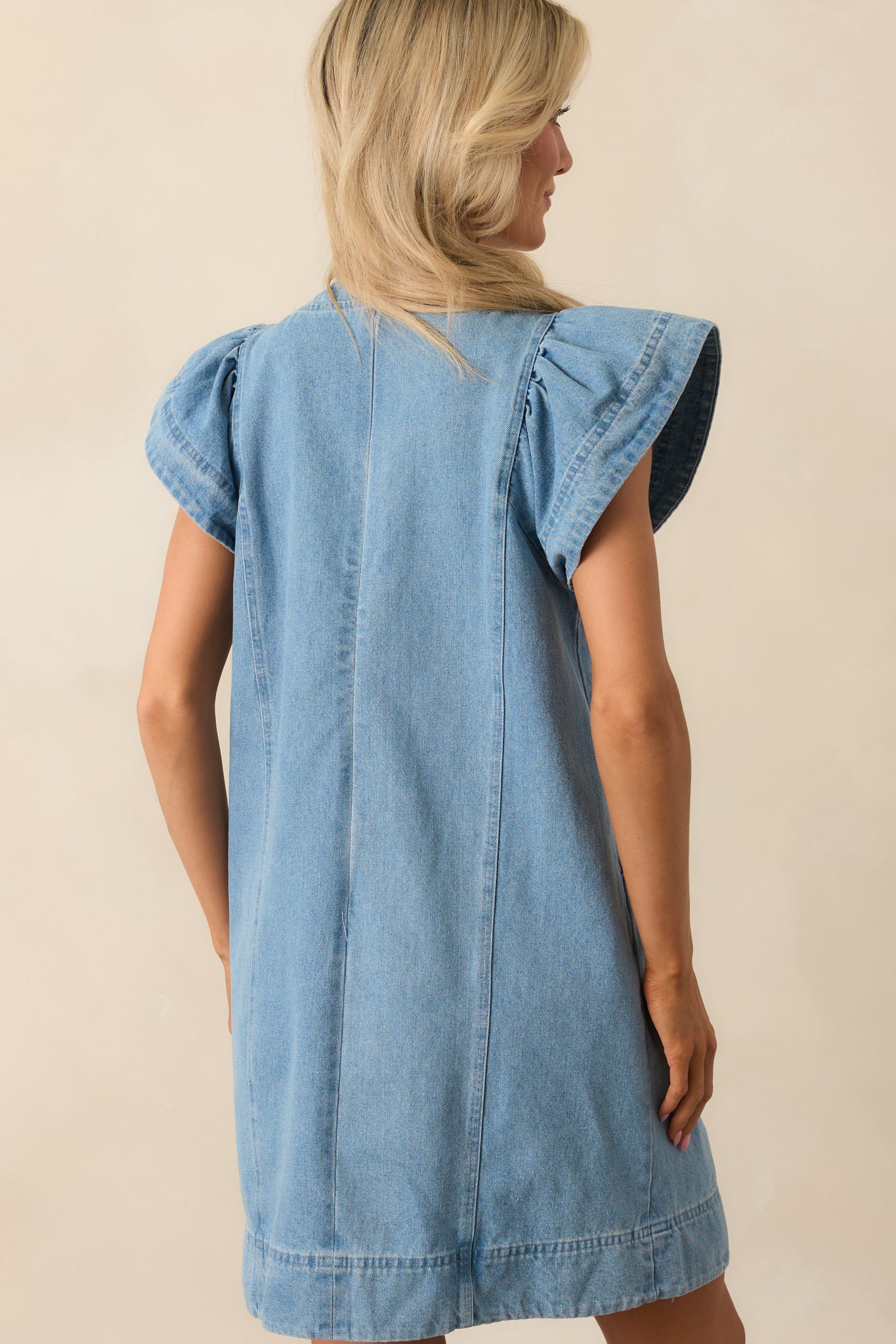 A back view of the denim mini dress highlighting the clean paneled design and structured fit.