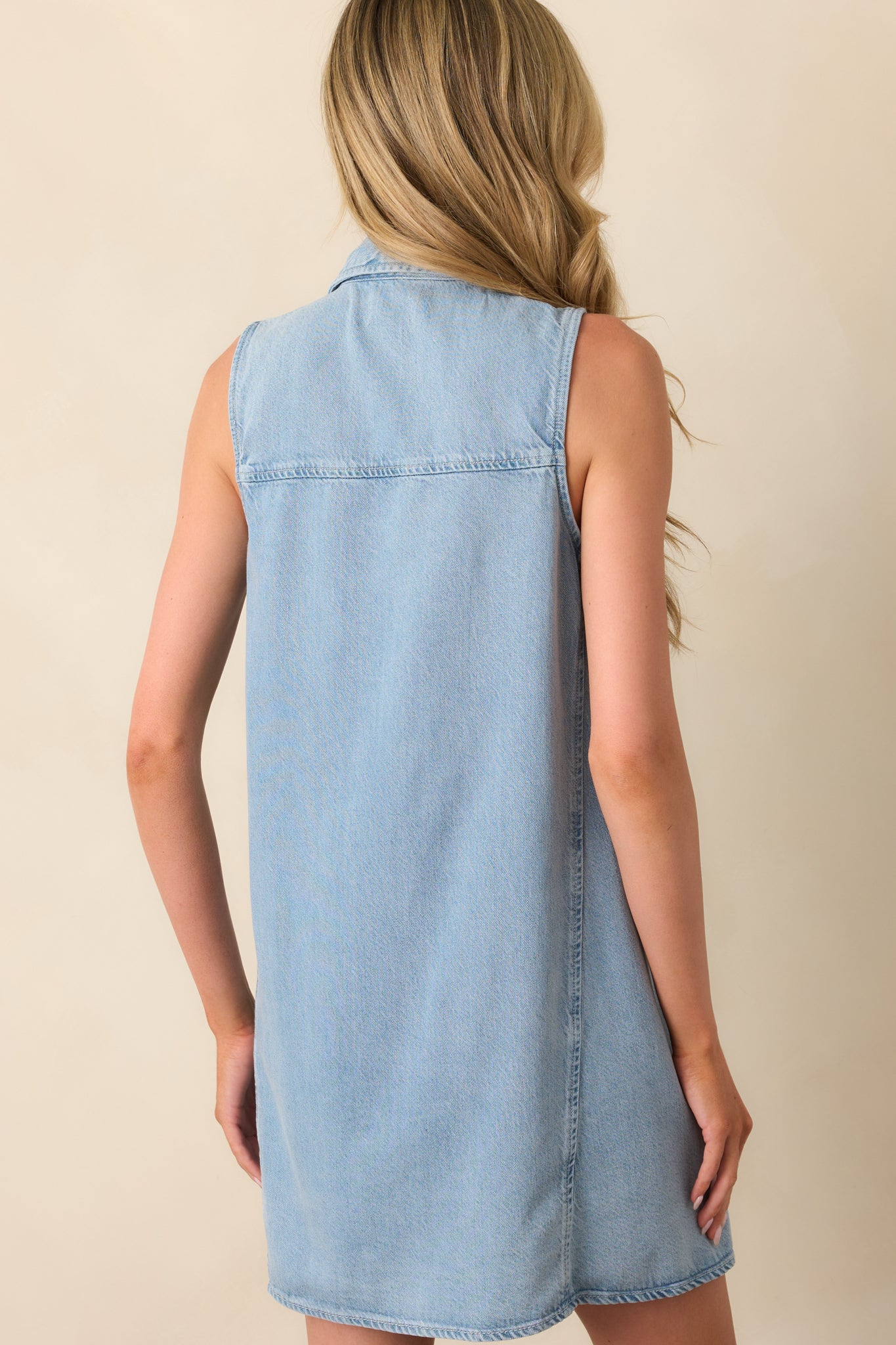 A view from behind showing the dress’s sleeveless cut, panelled back design, and relaxed fit in light wash denim.