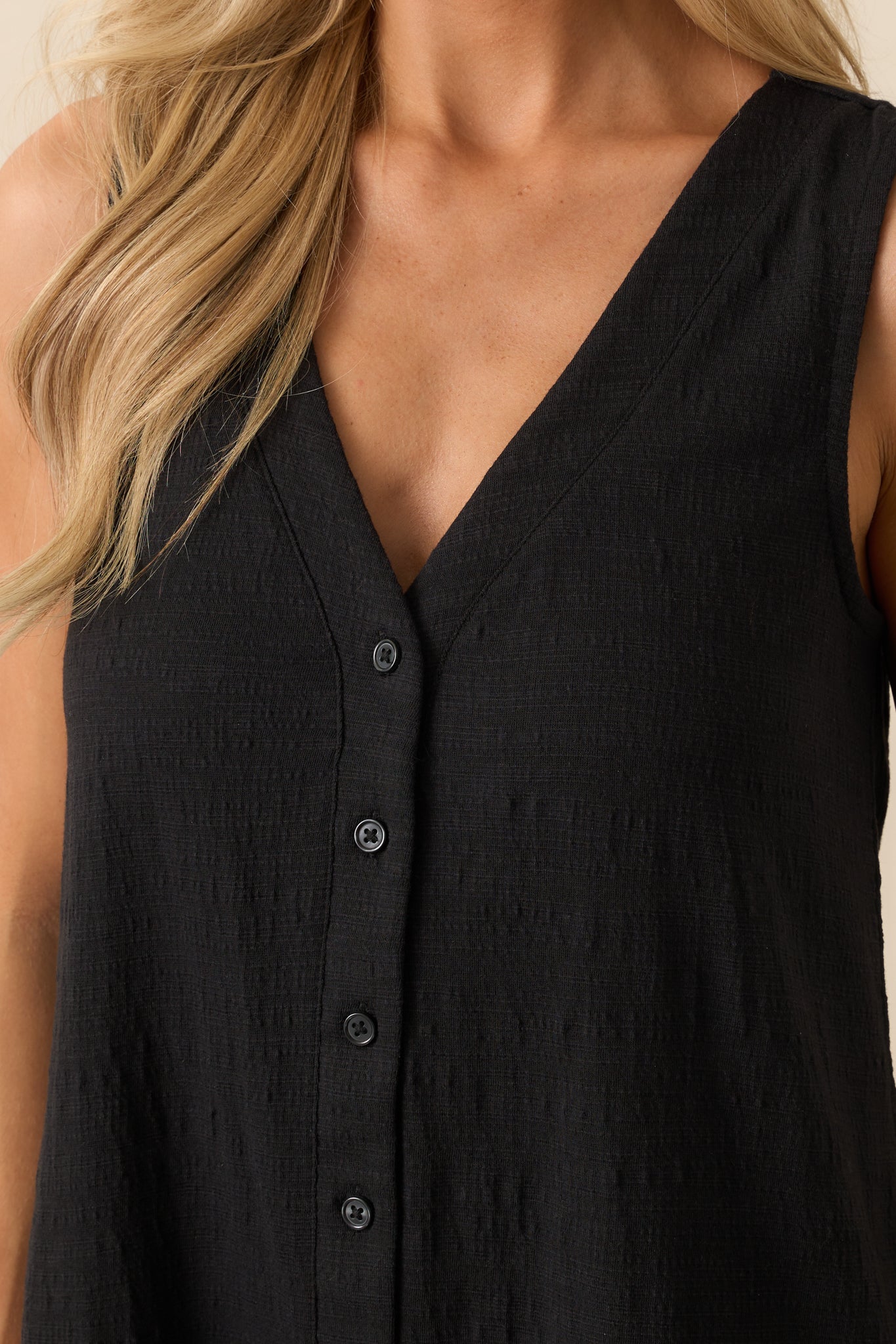 Close-up of the textured fabric and button detailing on the front of the black romper.