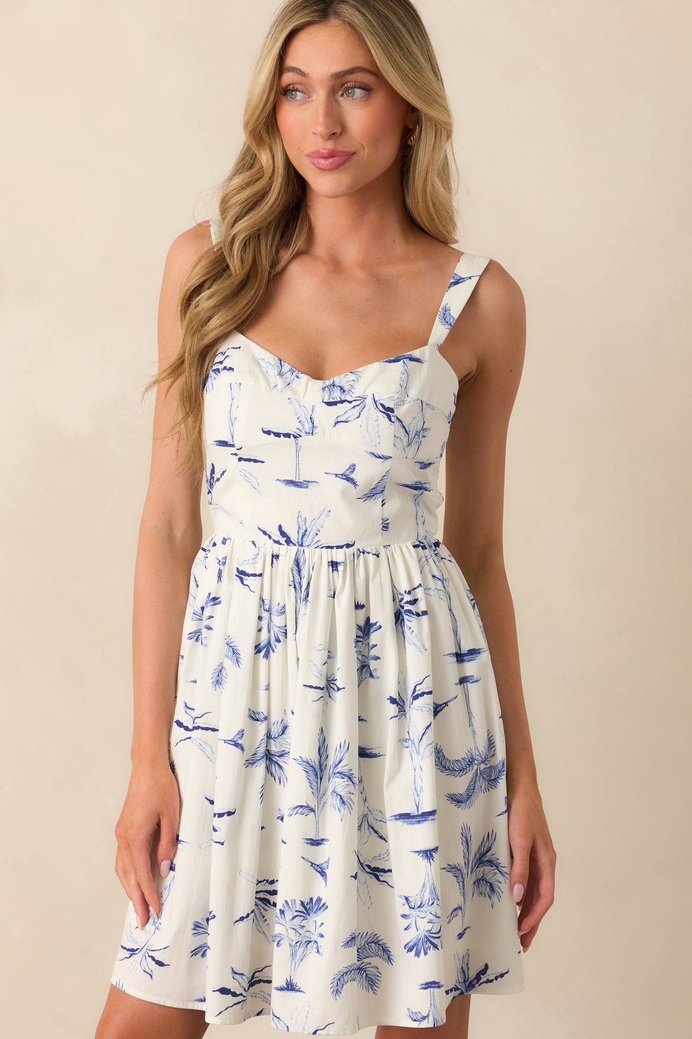 Front view of a mini dress with a blue watercolor palm tree print and a sweetheart neckline.