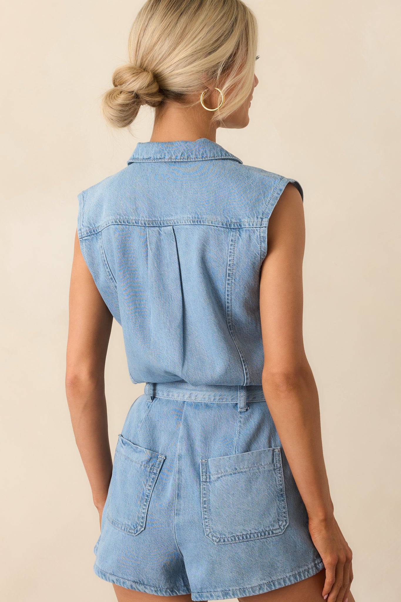 A view from behind showing the romper’s sleeveless cut, panelled back design, and relaxed fit in light wash denim.