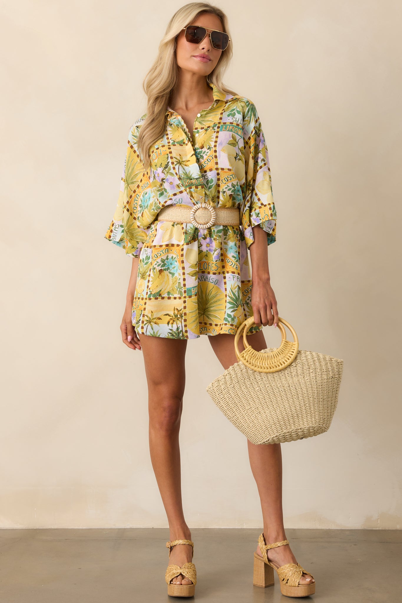 Full-length view of a yellow romper with a vibrant watercolor-style tropical fruit print and a collared neckline.