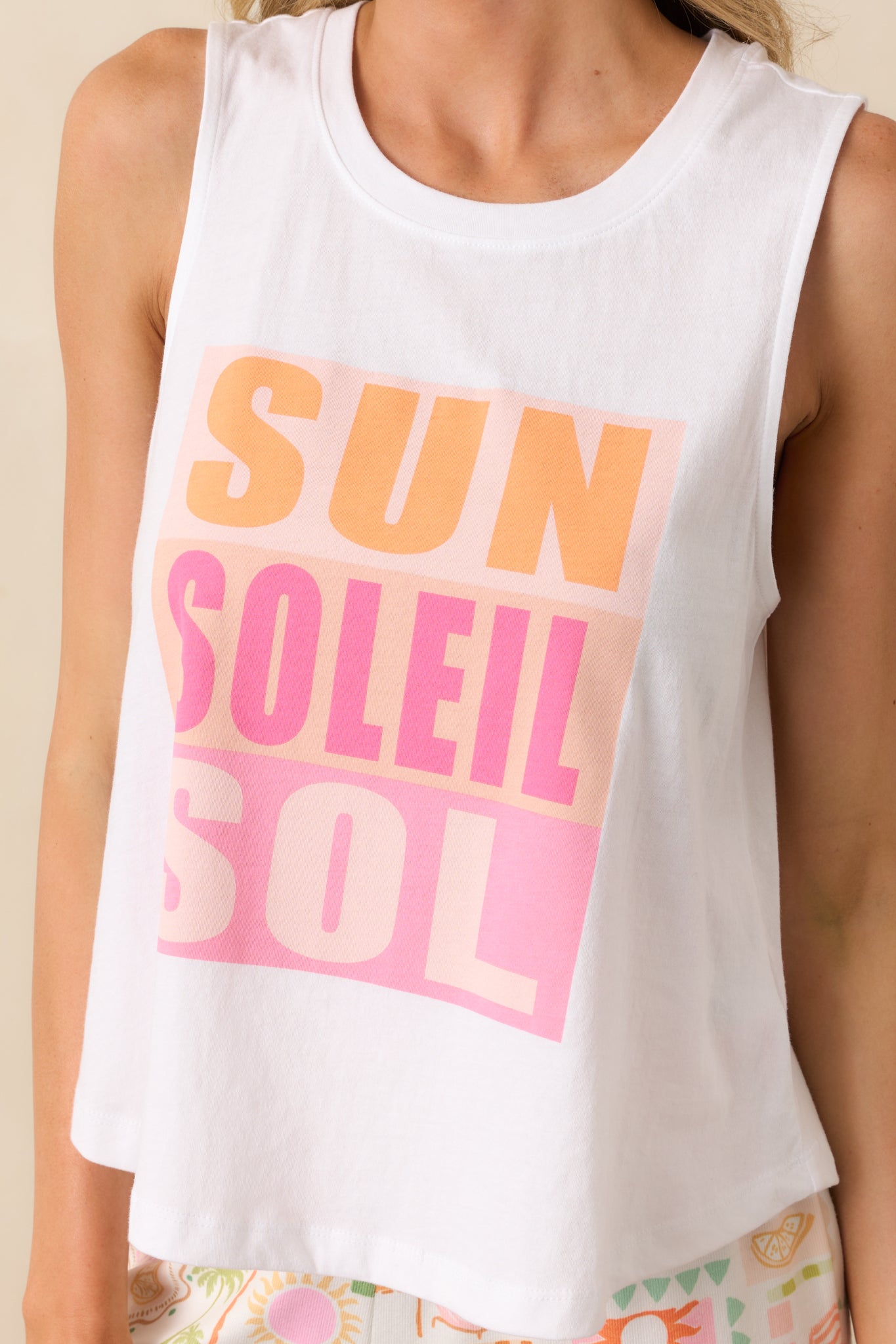 Close-up of the "Sun Soleil Sol" multicolor graphic print on the white tank top fabric.