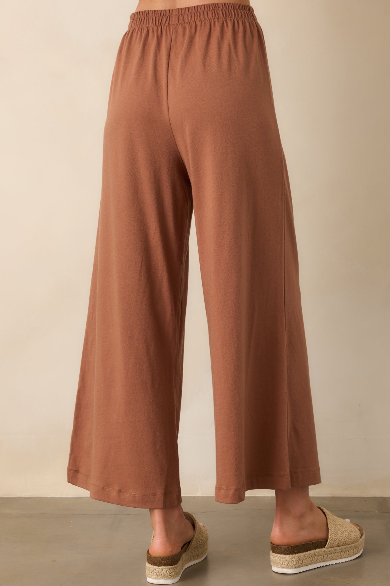 Rear view of the brown pants showing the elastic waistband and relaxed wide-leg design from behind.