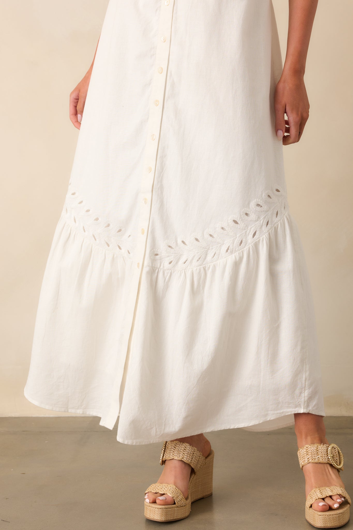 Detailed view of the bottom hem of the white maxi dress, highlighting the intricate eyelet embroidery and scalloped edge.