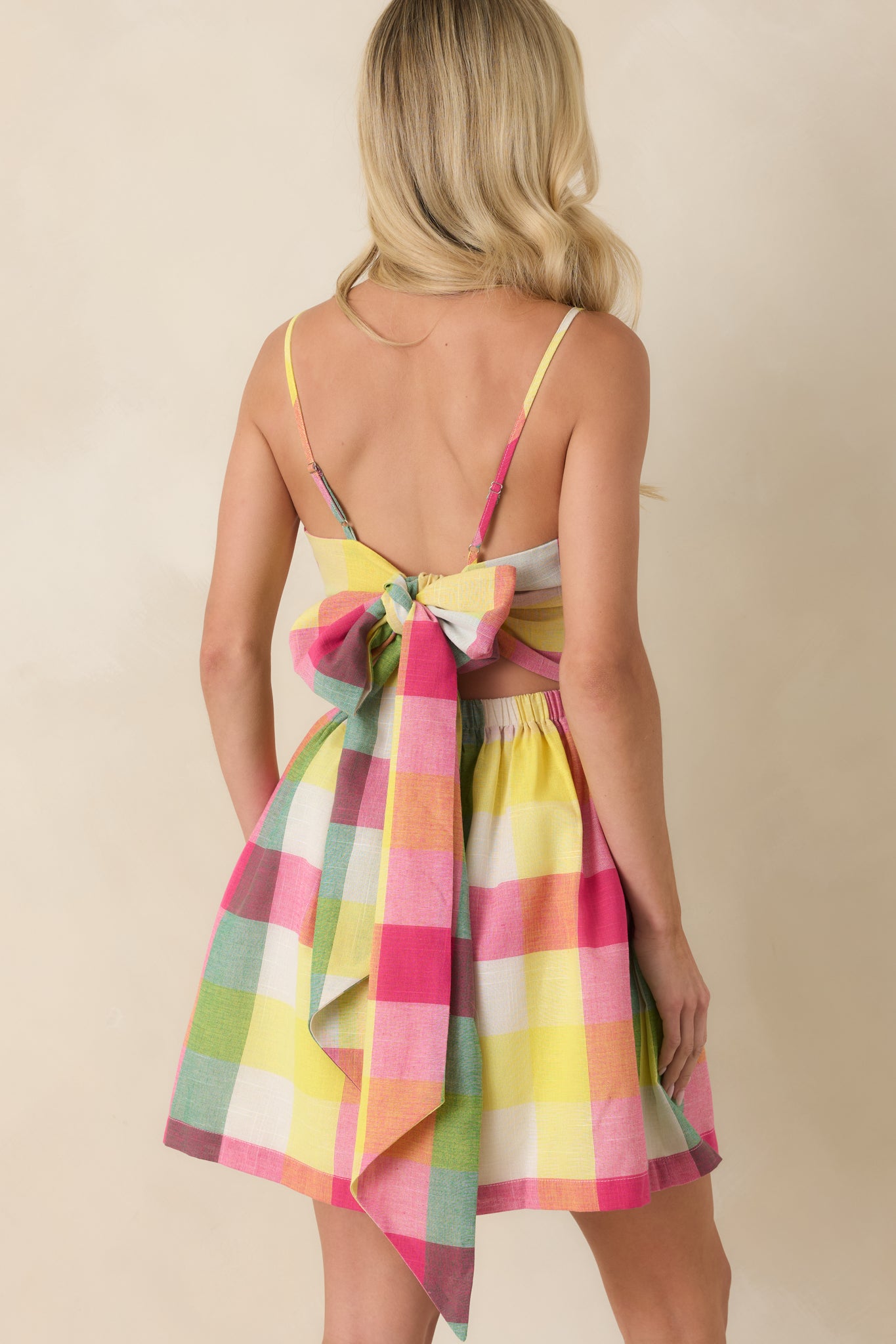 Rear view of the multi plaid mini dress featuring an open rear design with long adjustable tie details and a flared skirt silhouette.