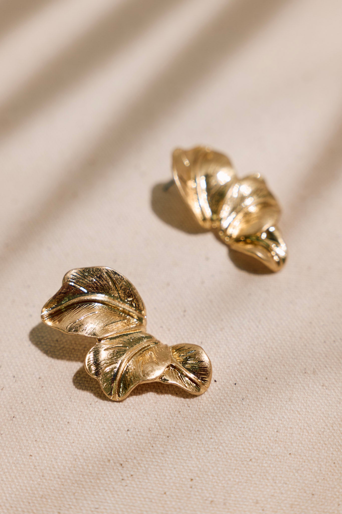Detailed close-up of gold earrings showcasing three palm leaf elements, worn gold finish, and secure post backing.