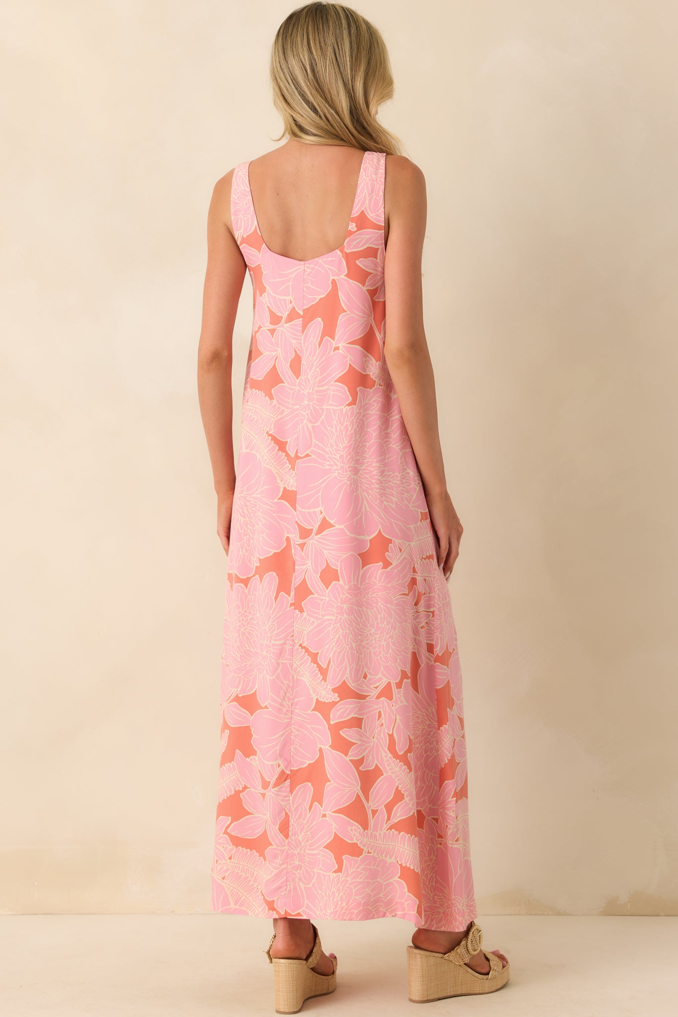 A view from behind of the pink coral maxi dress, revealing the sleeveless design, mini length lining, and the flowy shape of the skirt from the back.