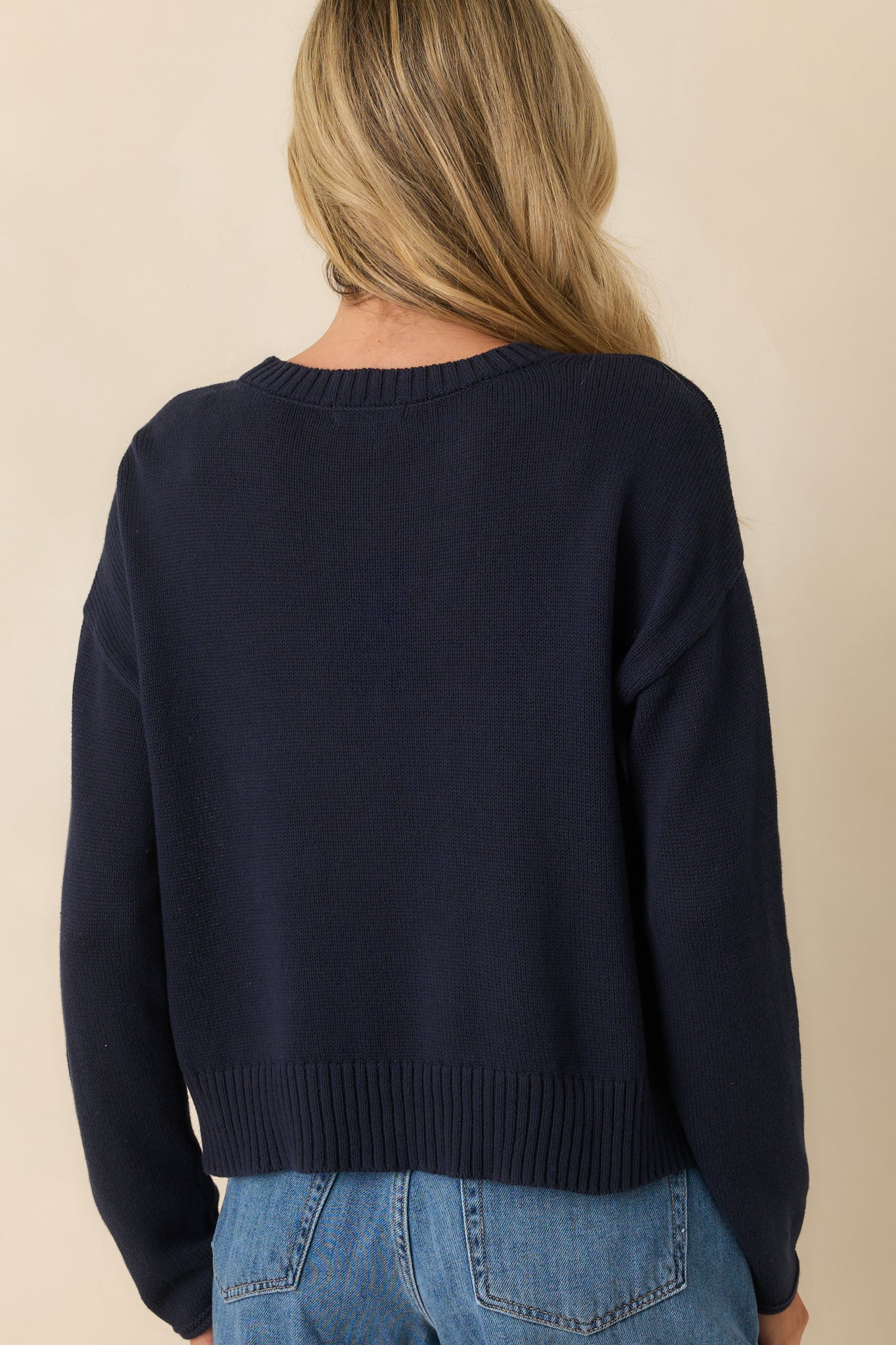 Back view of the navy sweater showing the solid knit design with no graphic and the rolled finish on the sleeve hems.