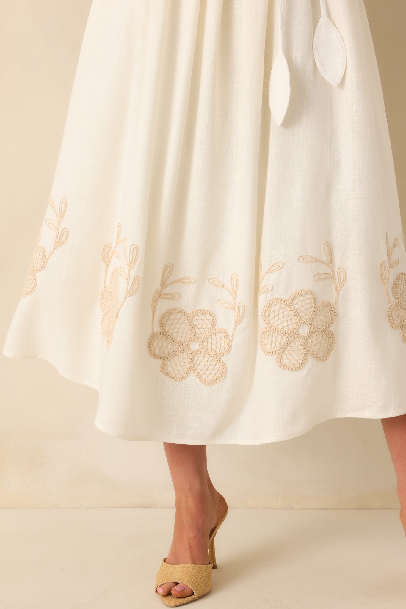 Close-up of the lower skirt showing the beige floral embroidery along the hem and the textured linen blend fabric, with a glimpse of the full ivory lining beneath.